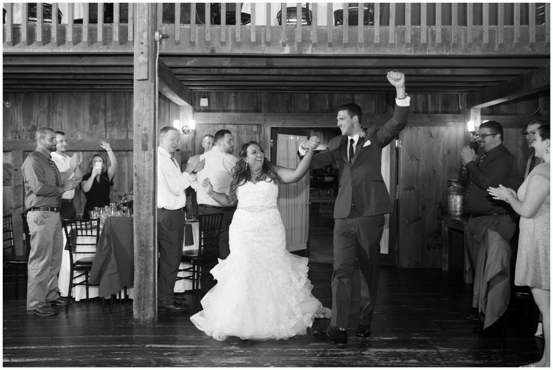 Wedding guests dance in a rustic hall, with the bride and groom at center and guests clapping around them