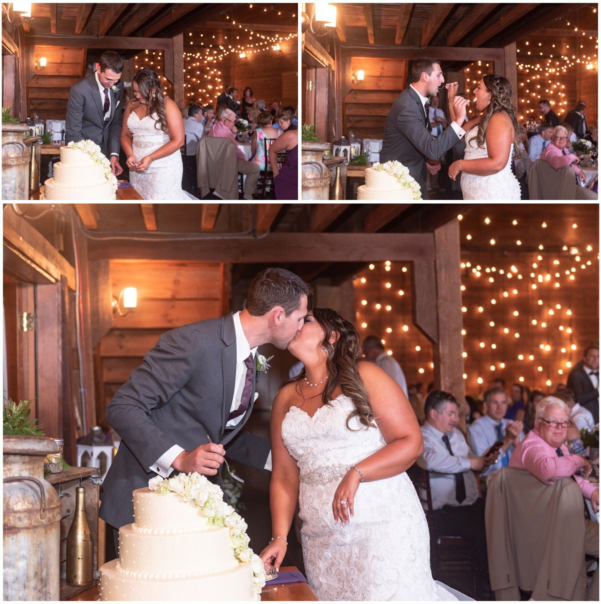 Bride and groom kissing beside wedding cake in a warmly lit reception hall