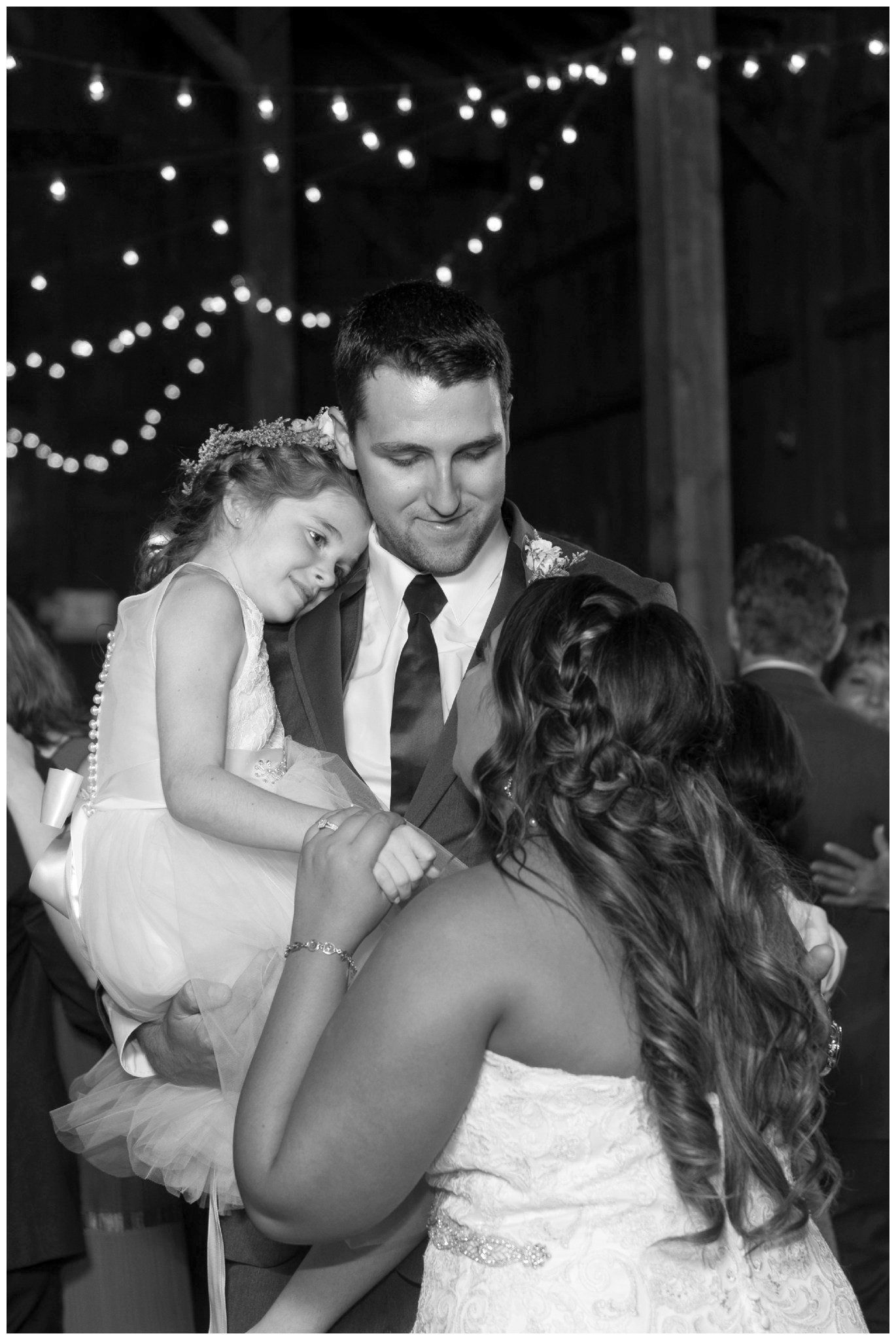 Man in a suit dancing with two women at a nighttime celebration under string lights