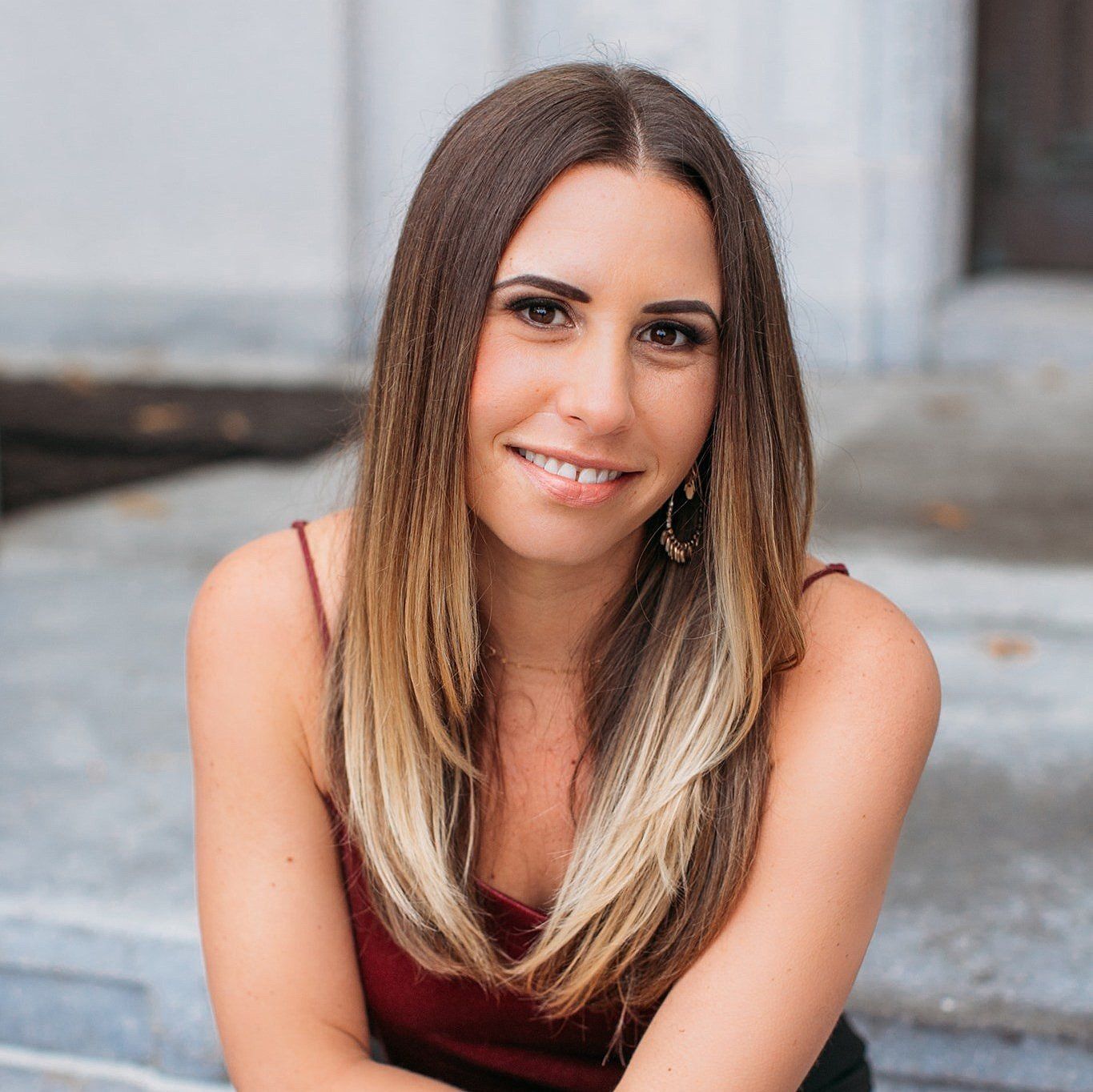 Smiling woman with long brown hair sitting on steps in a maroon top