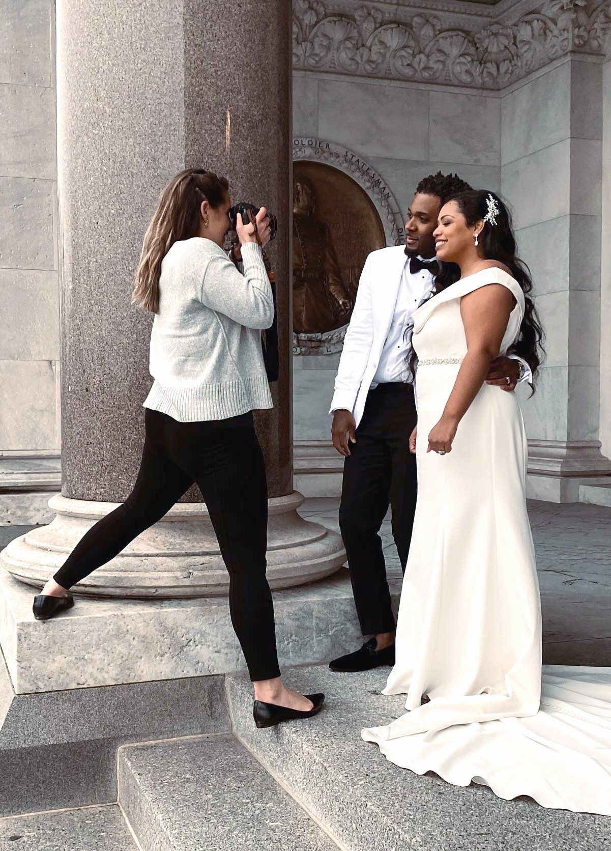 Photographer capturing a couple in wedding attire on stone steps at an ornate building entrance