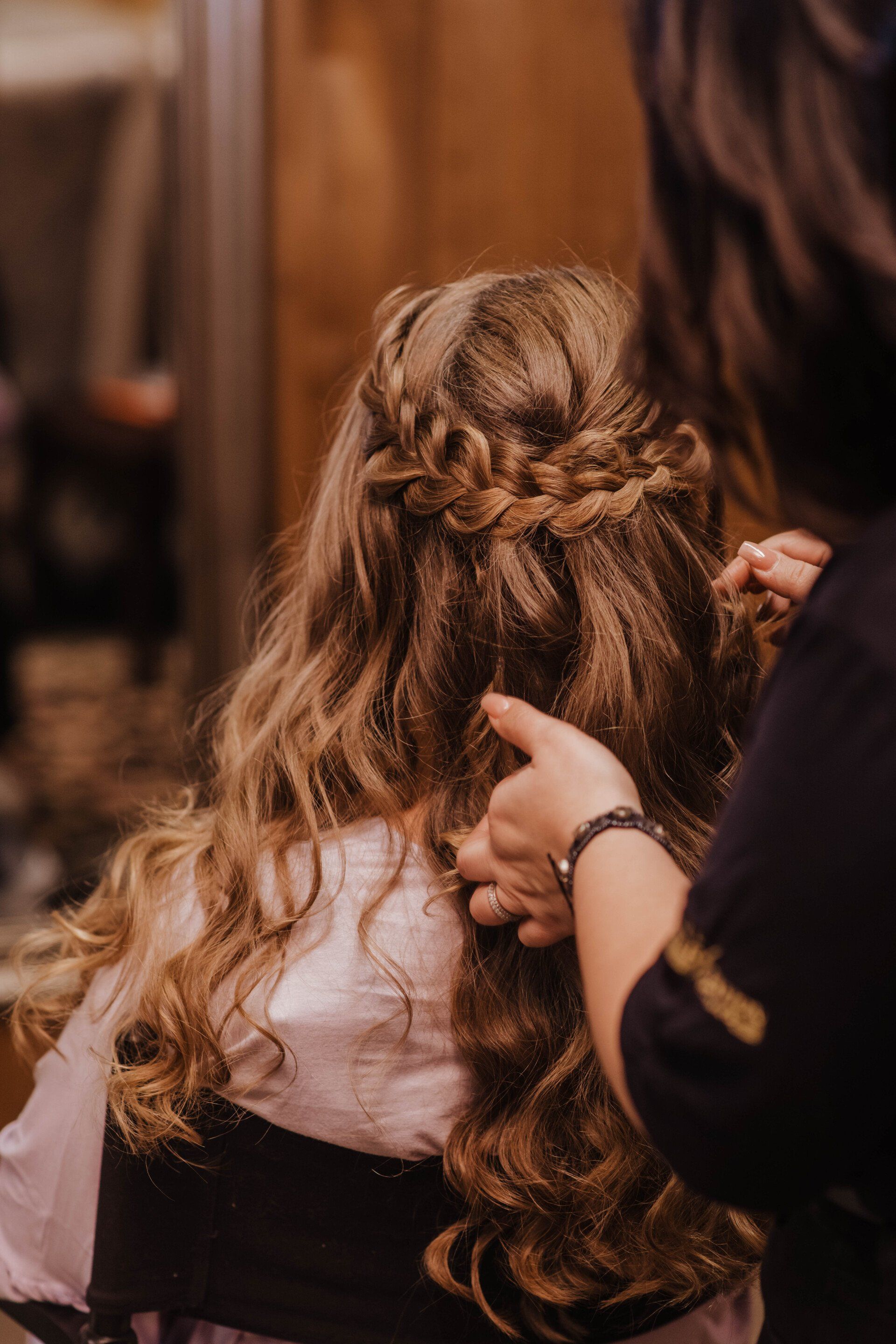 Stylist braiding long curly hair in a warm indoor setting