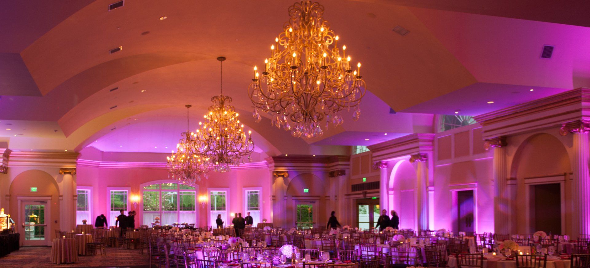 Elegant banquet hall with chandeliers and pink-purple uplighting, set for a formal event