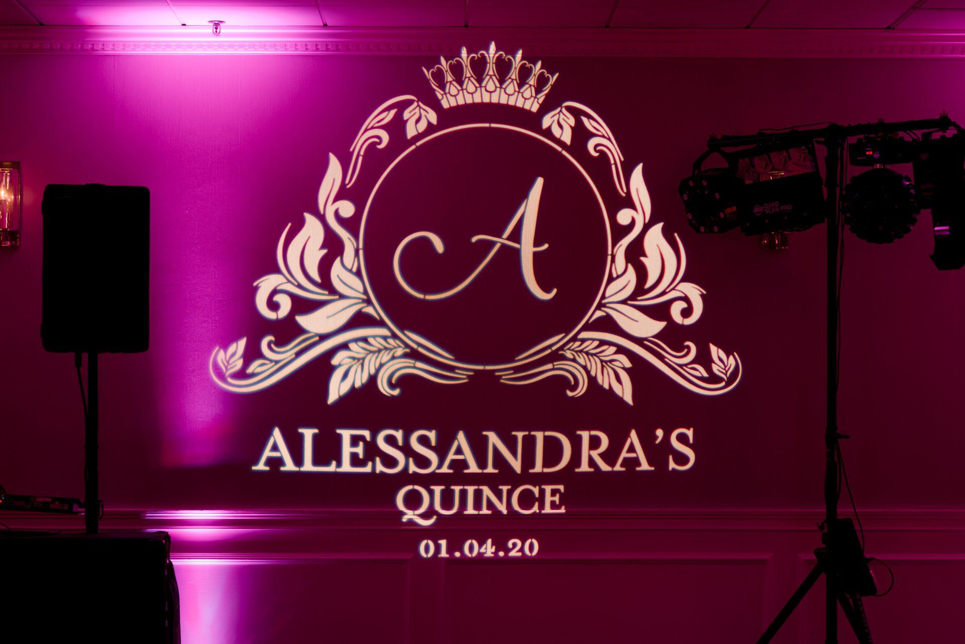 Pink-lit quinceañera backdrop with crown monogram and the text “Alessandra’s Quince 01.04.20”