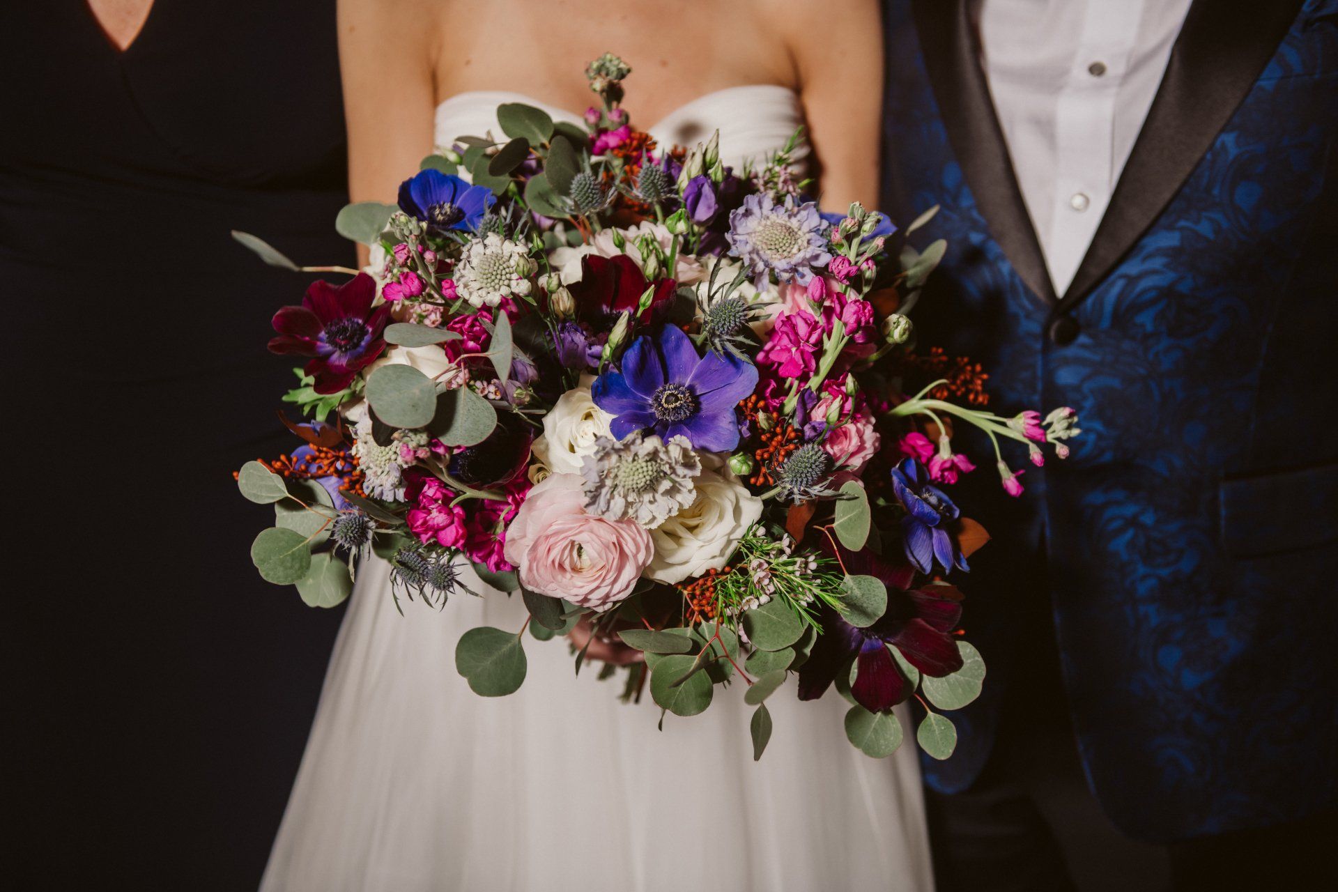 Bride and groom holding a vibrant bouquet of pink, purple, and white flowers