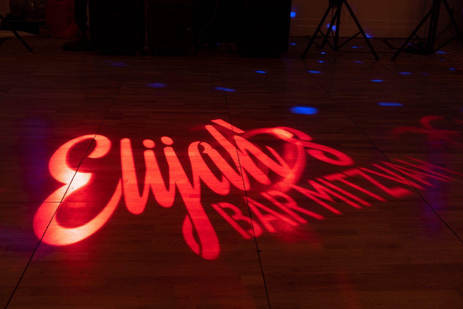 Red neon script sign reading “Eli’s Bar,” glowing on a dark floor indoors