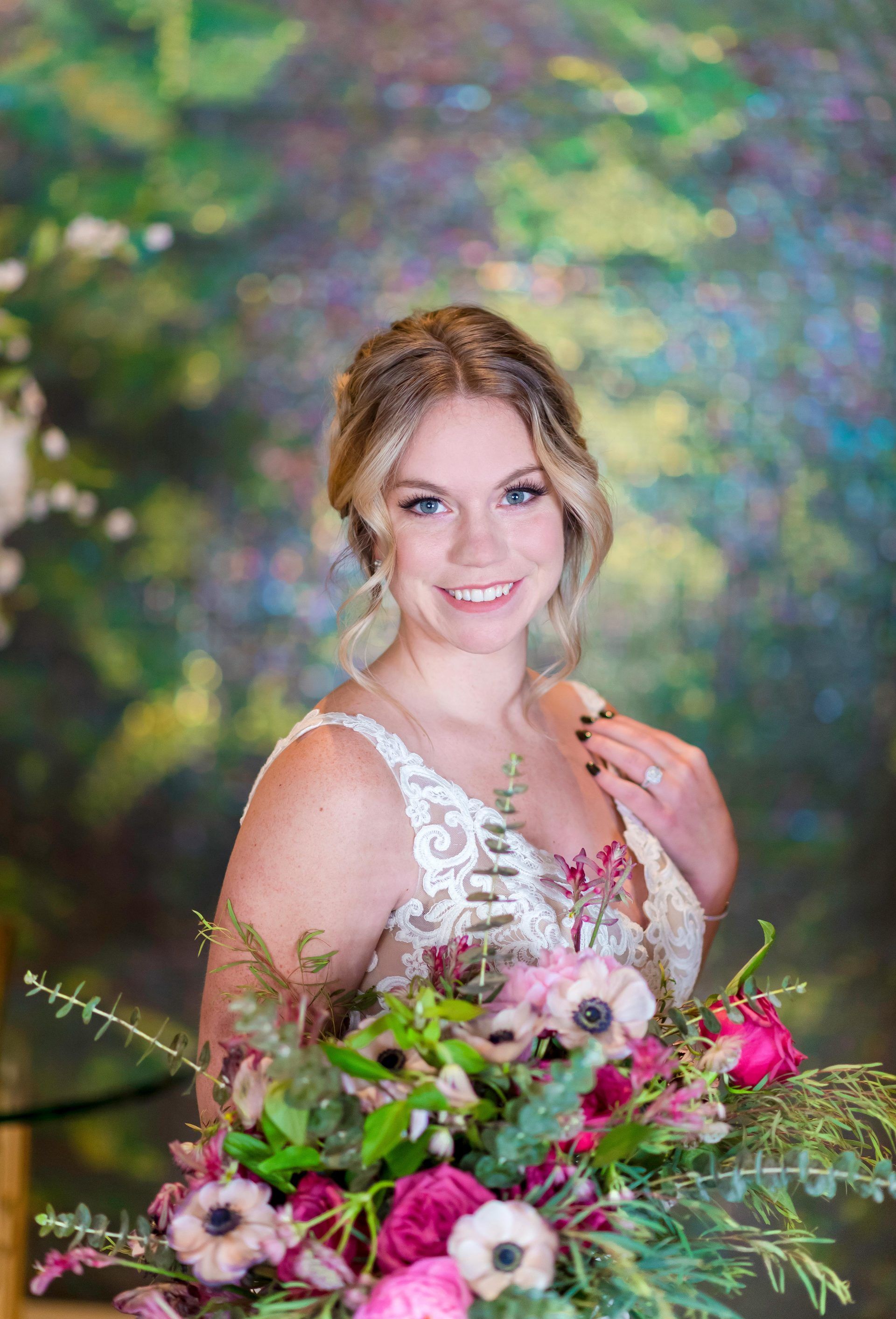 Smiling bride holding a pink-and-white bouquet against a colorful blurred garden backdrop