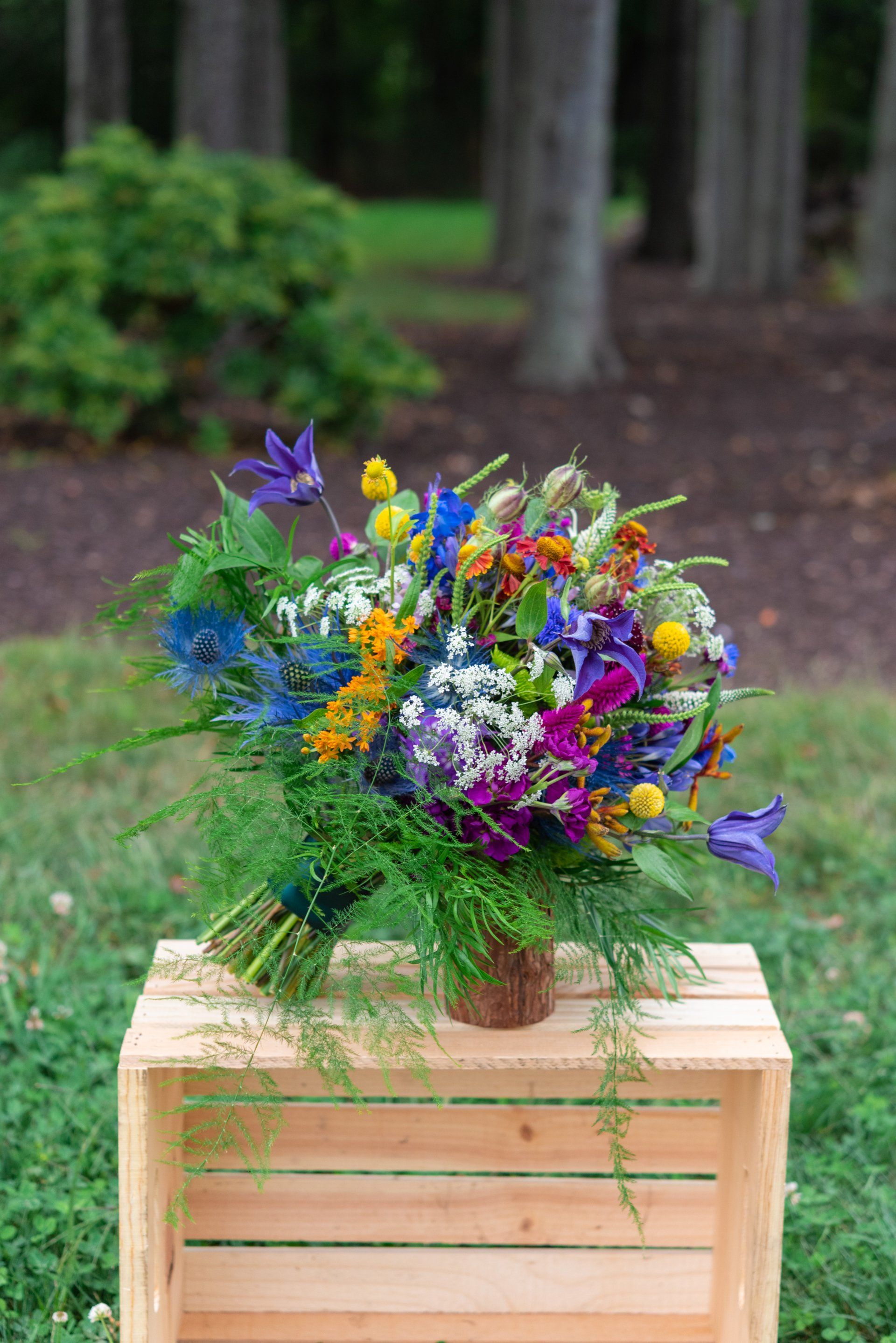 Colorful wildflower bouquet in a wooden crate outdoors against a blurred forest backdrop