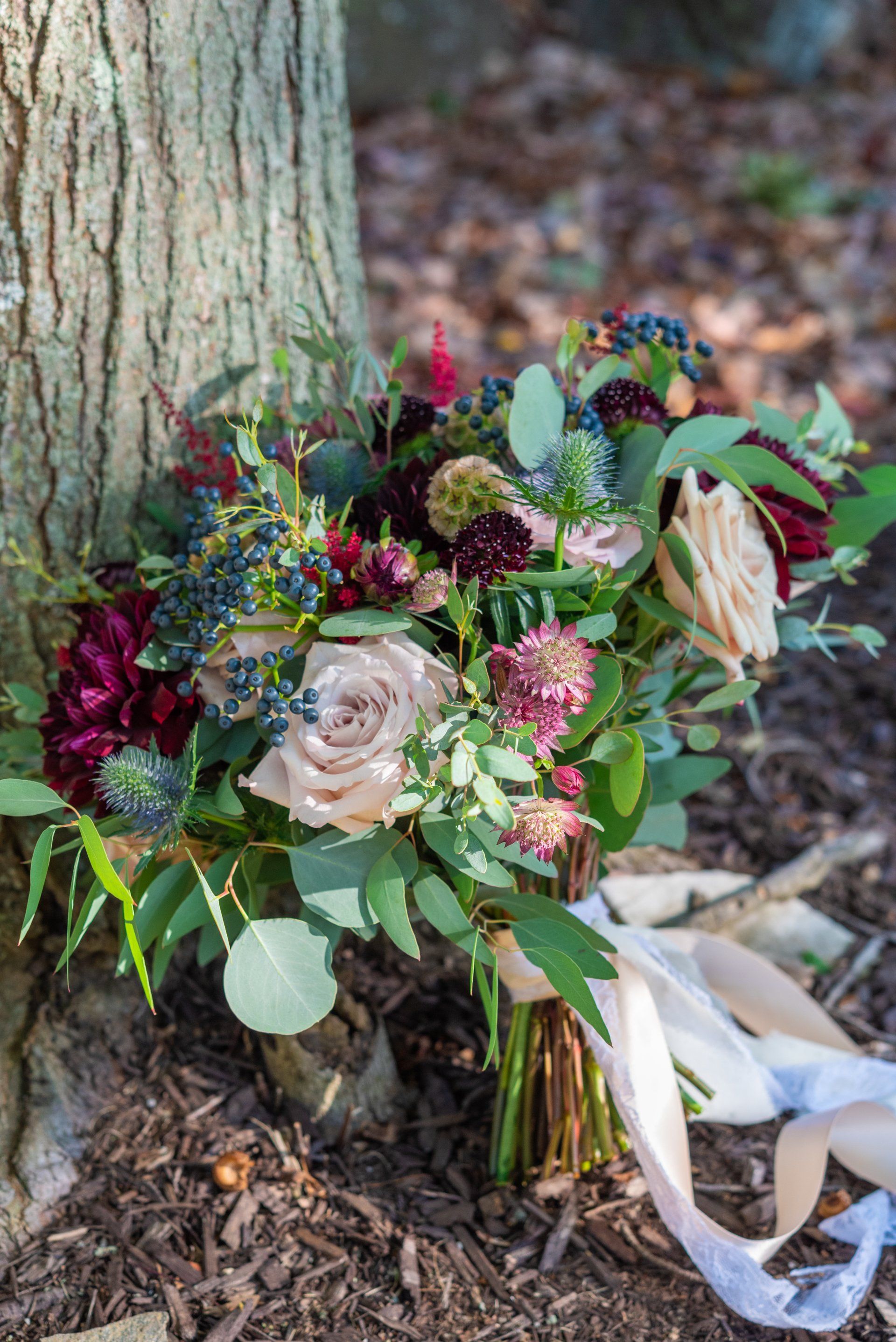 Floral bouquet with pink and burgundy flowers and greenery at the base of a tree outdoors