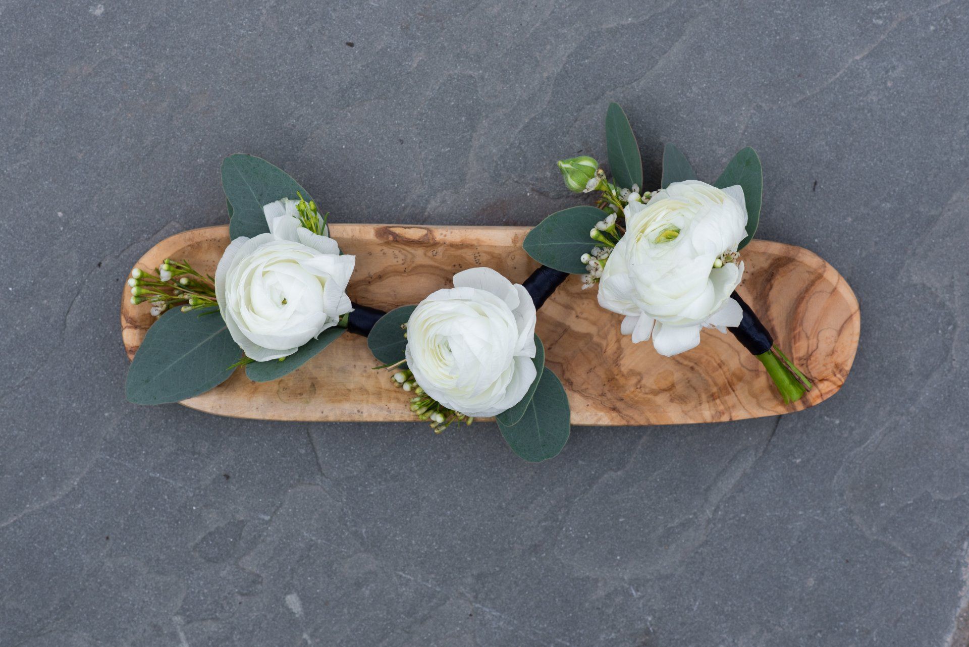 White flowers with greenery arranged on a small wooden tray over a gray surface