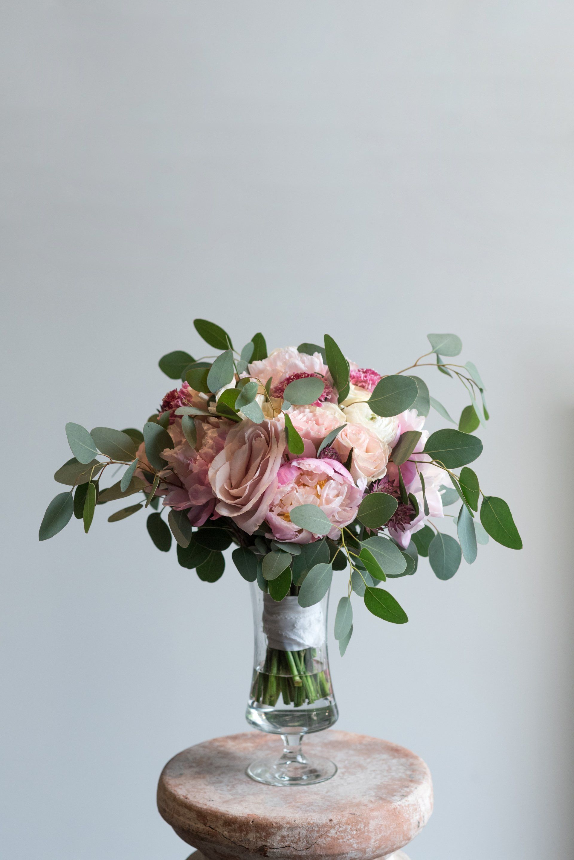 Pink floral bouquet in a clear glass vase on a round table against a light gray wall