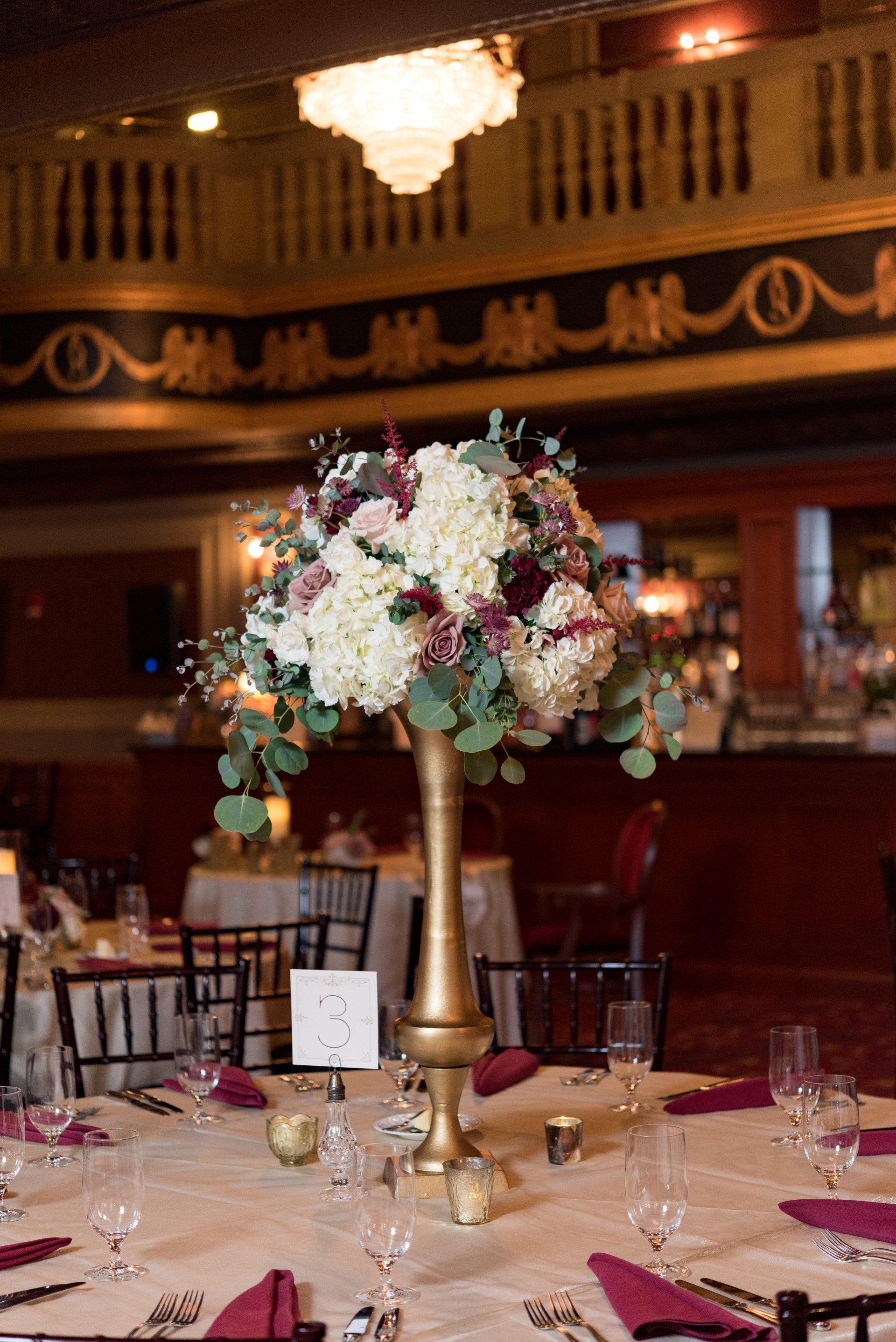 Elegant banquet table with tall floral centerpiece and set place settings in a warm-lit ballroom
