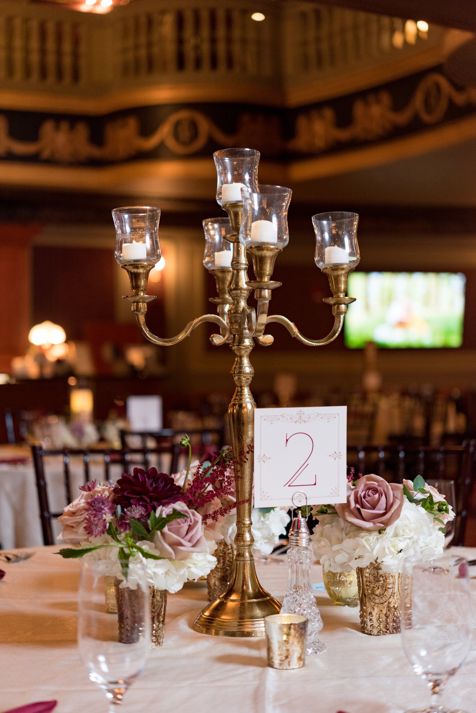 Elegant banquet table with a gold candelabra, white linens, and floral centerpiece in a softly lit hall