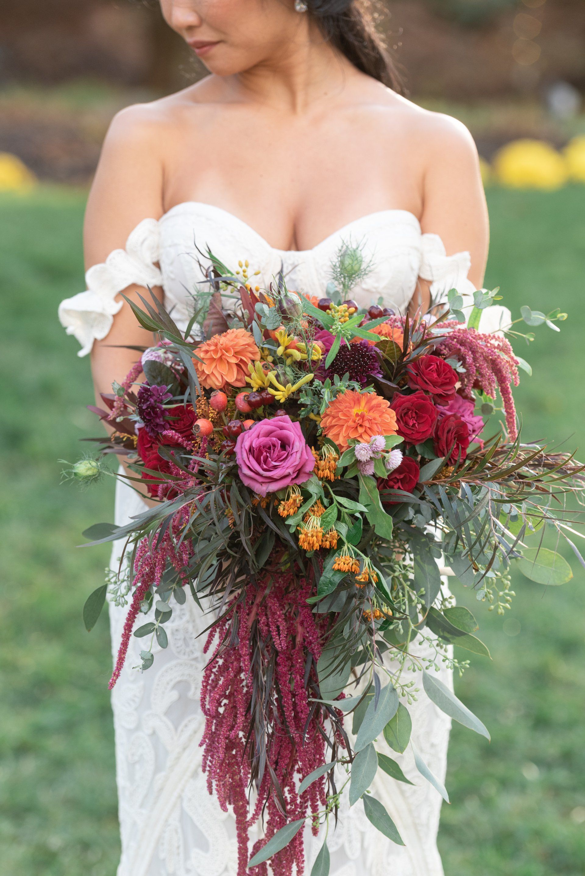 Bride holding a vibrant bouquet of pink, orange, and burgundy flowers with trailing greenery