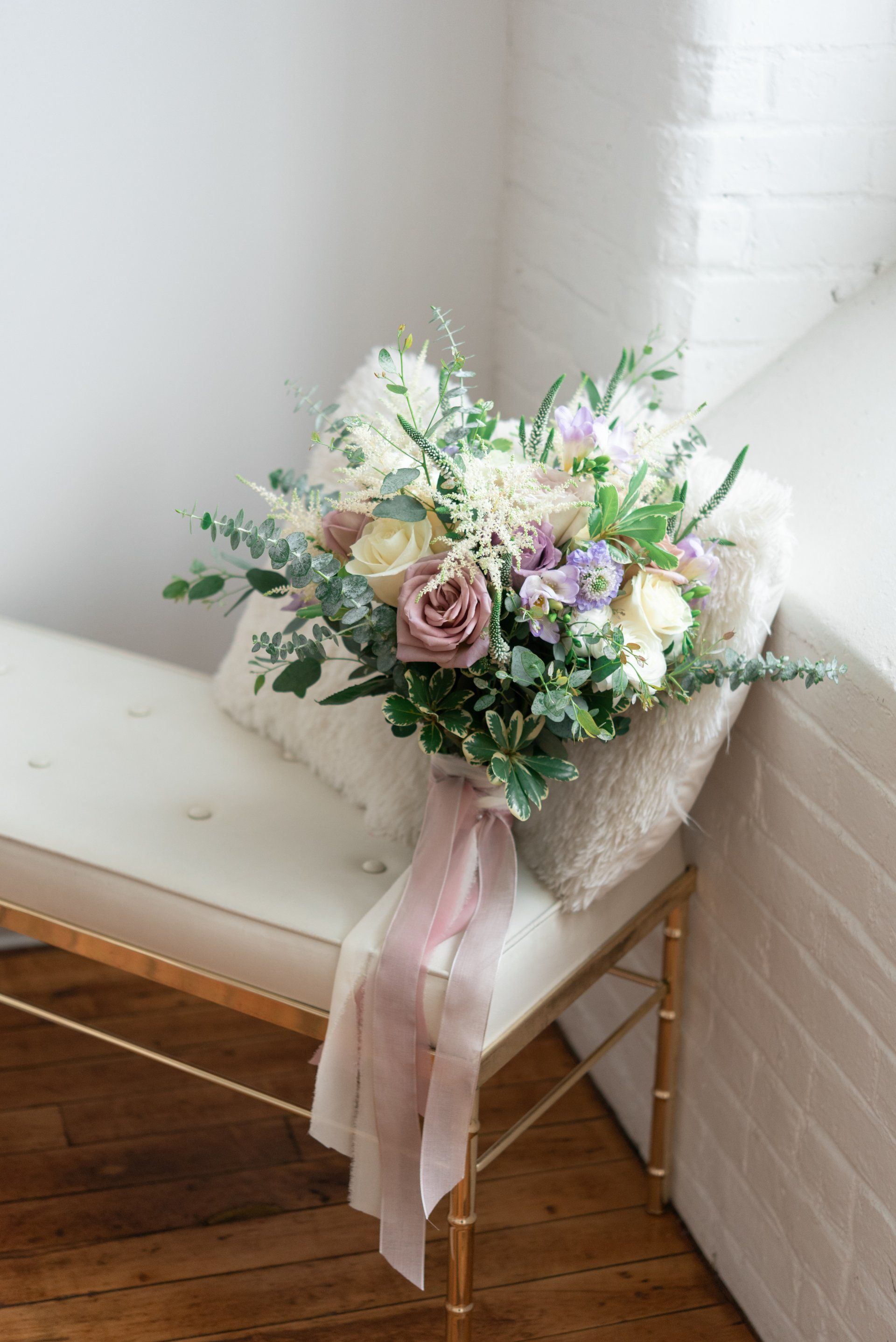 Pastel flower bouquet with pink ribbon on a white bench by a brick wall