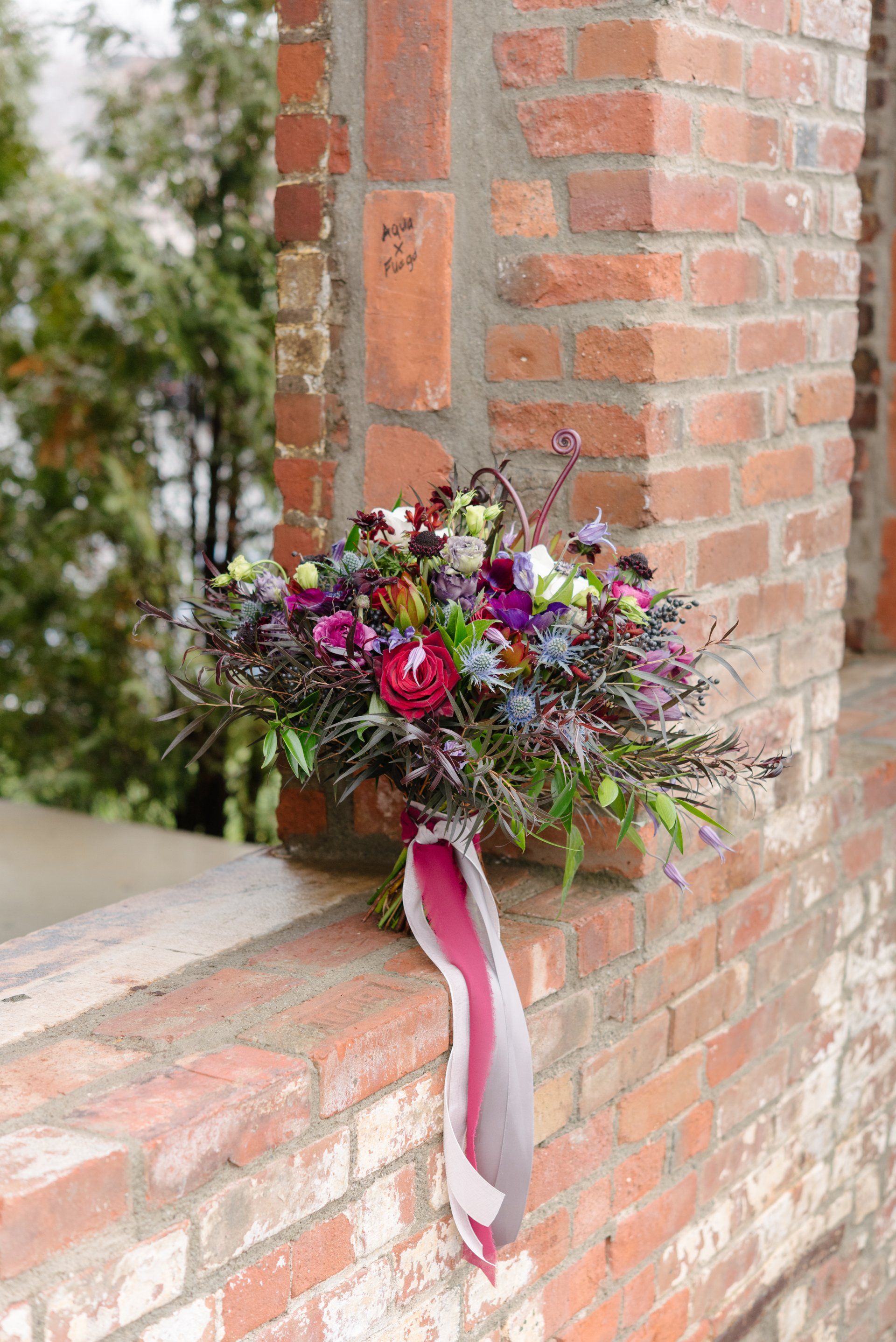 Colorful floral bouquet with pink ribbon on a brick ledge by a brick wall