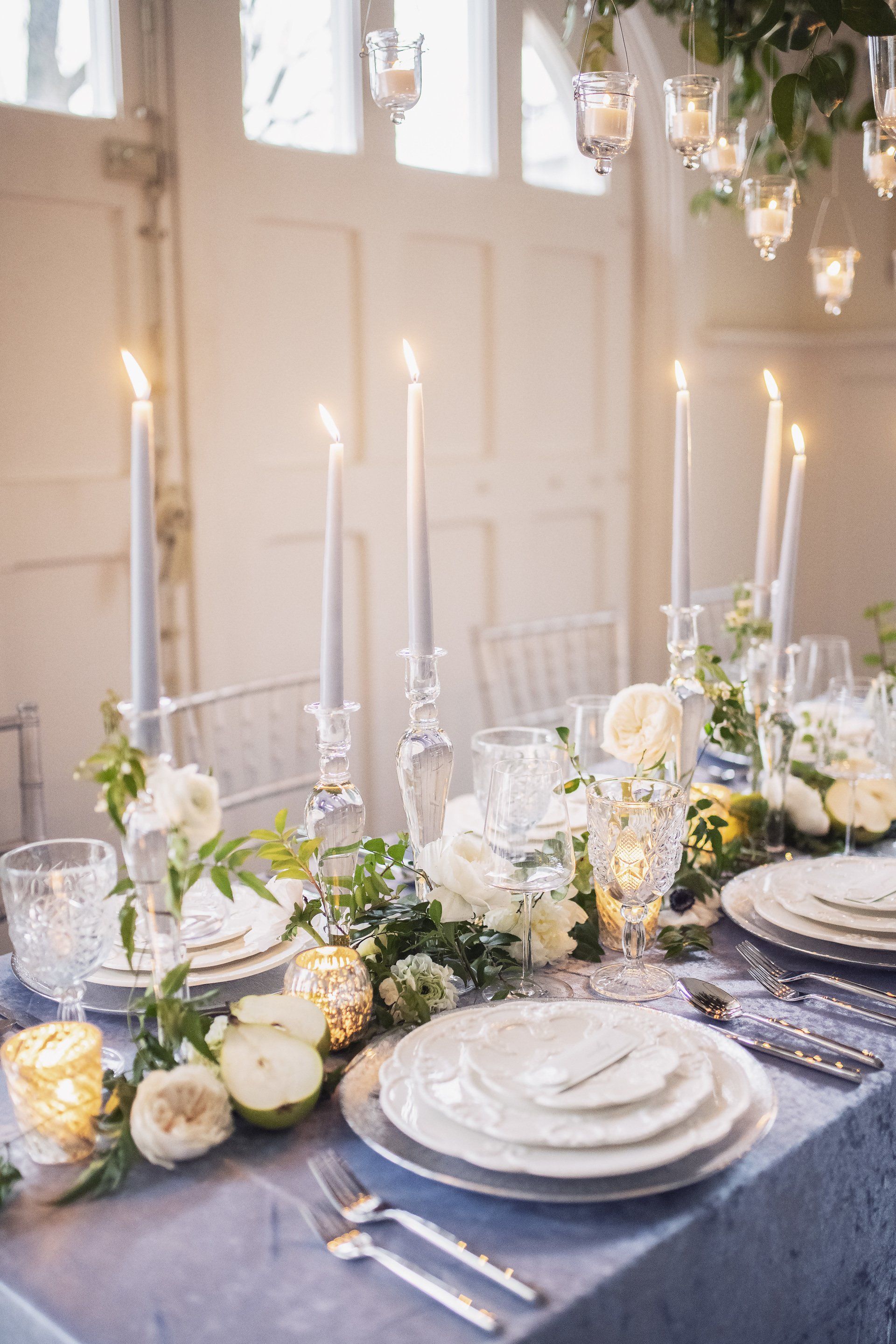 Elegant candlelit dining table with white plates, flowers, and glassware in a bright room