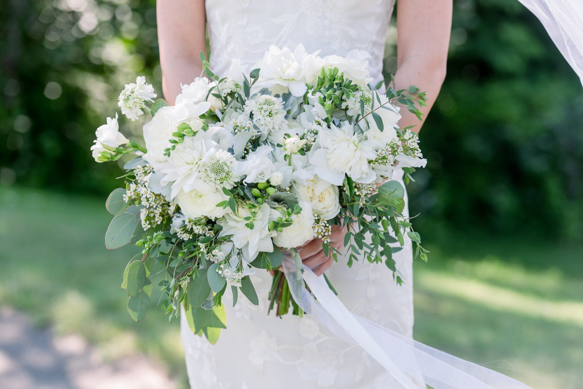 Bride holding a white-and-green wedding bouquet outdoors