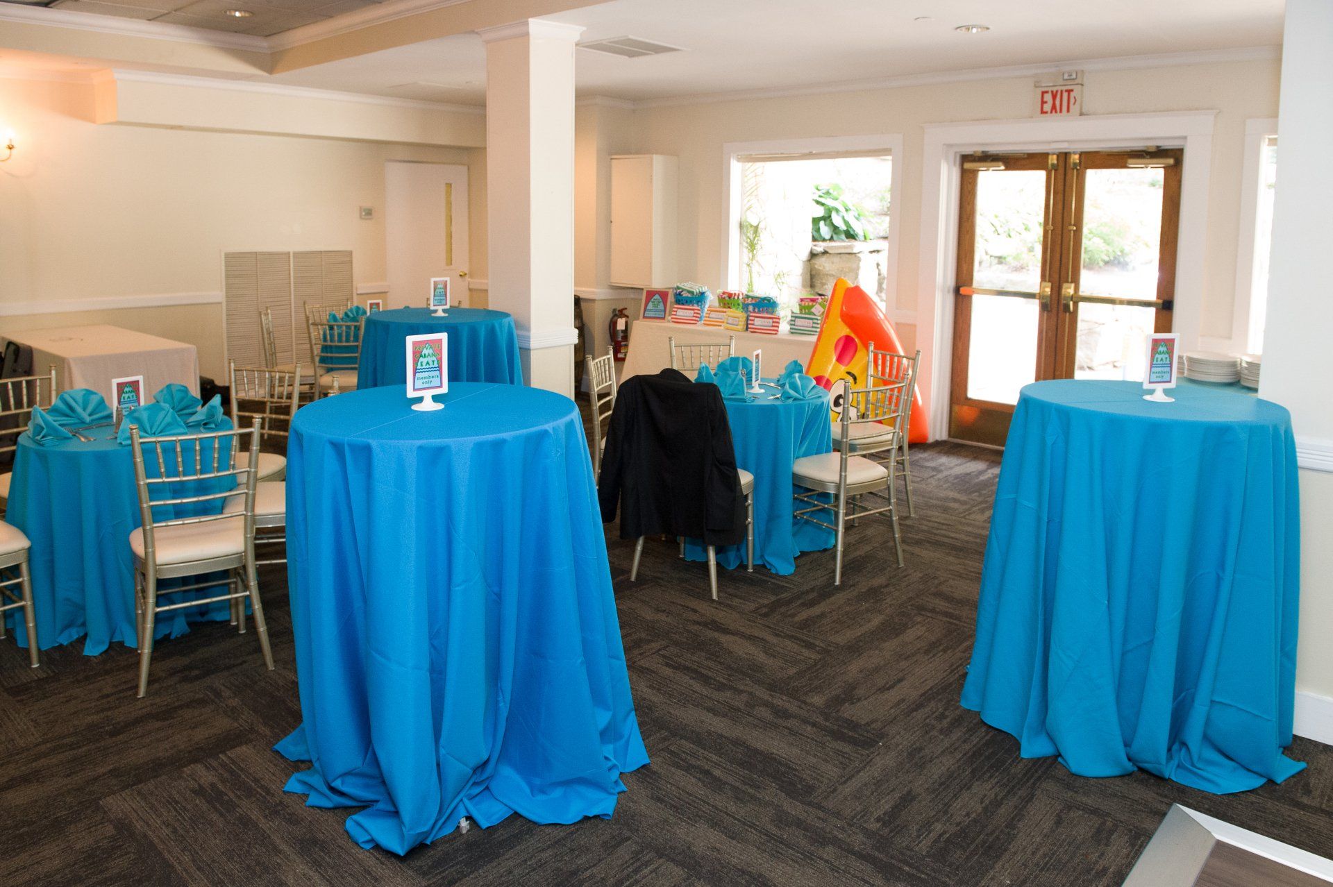 Event room with blue-draped tables, chairs, and a decorated table near glass doors