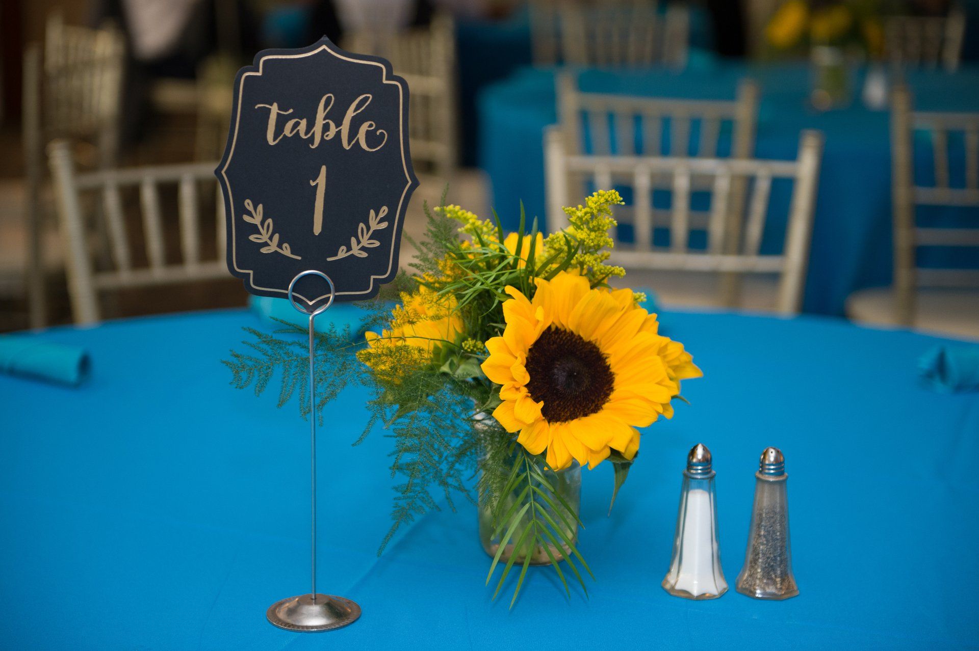 Table 1 sign beside a vase of sunflowers on a blue tablecloth at a banquet table