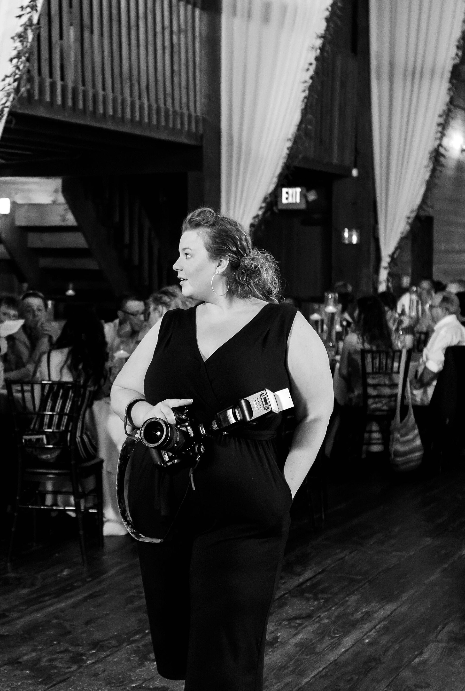 Person in a black dress with a camera around their neck stands in a busy indoor venue.