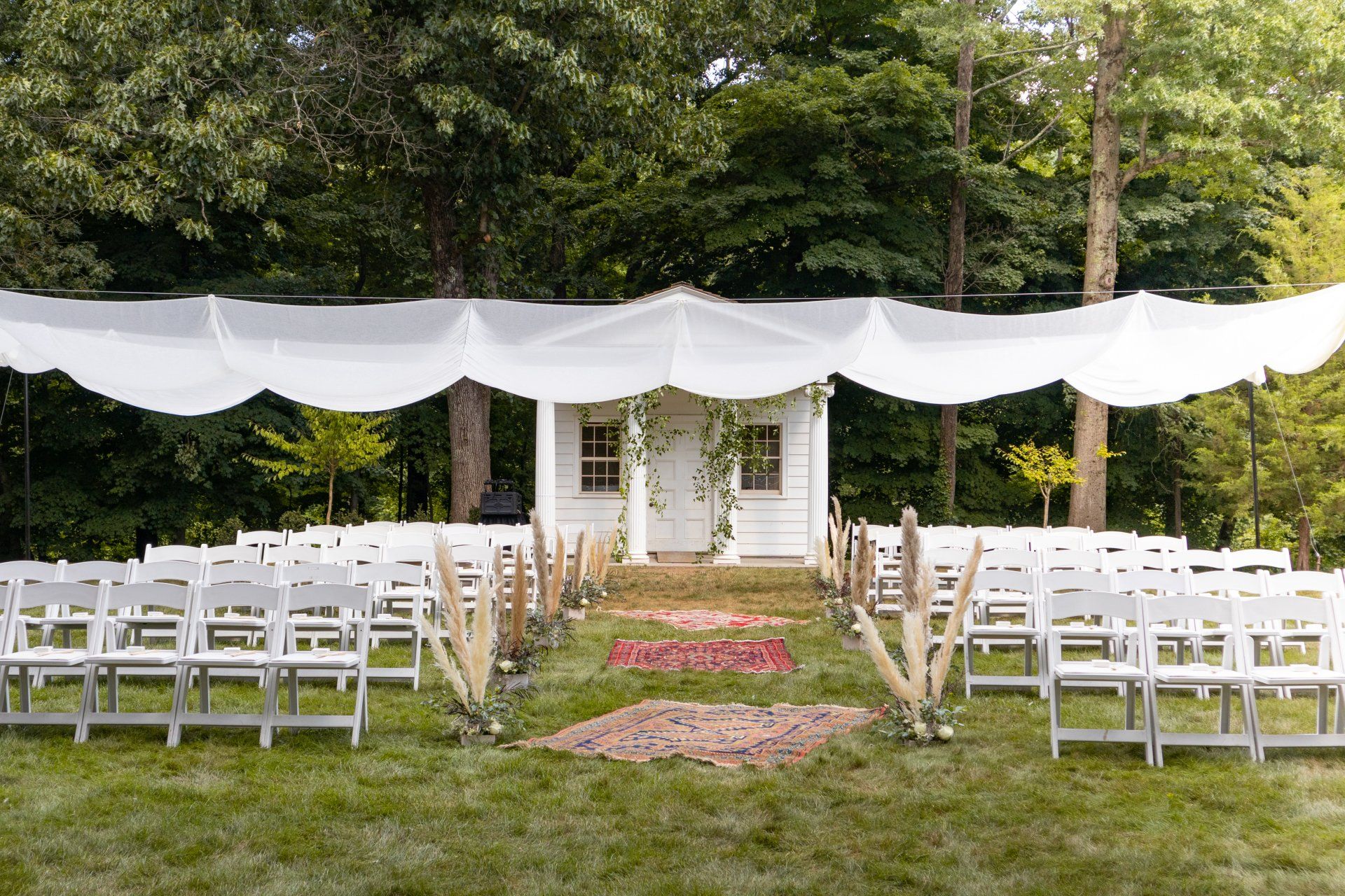 Outdoor wedding ceremony setup with white chairs under a white canopy in a garden