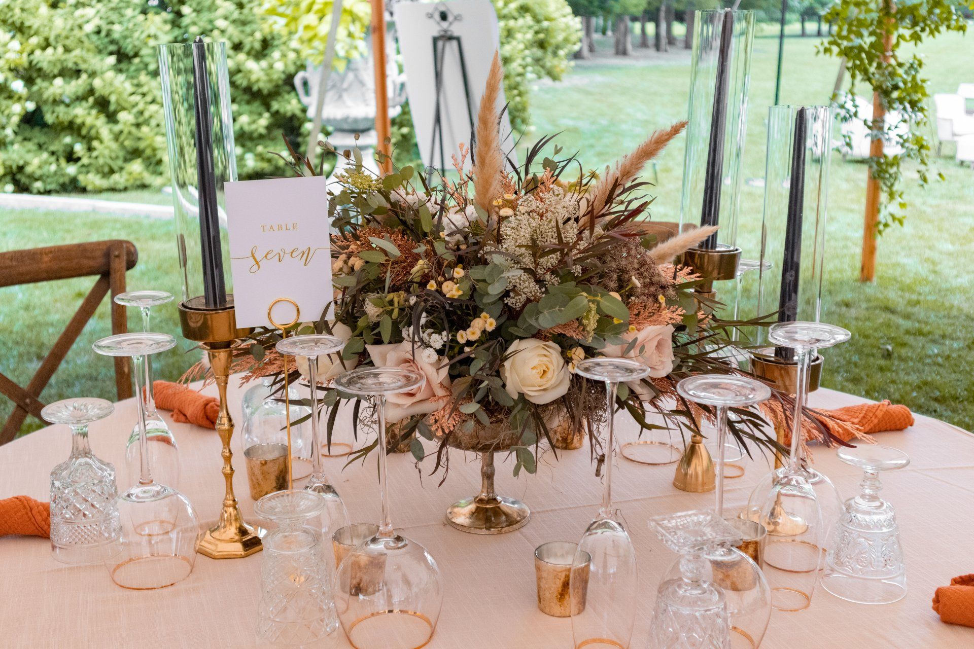 Elegant outdoor table setting with gold accents, glassware, and a floral centerpiece in a garden tent