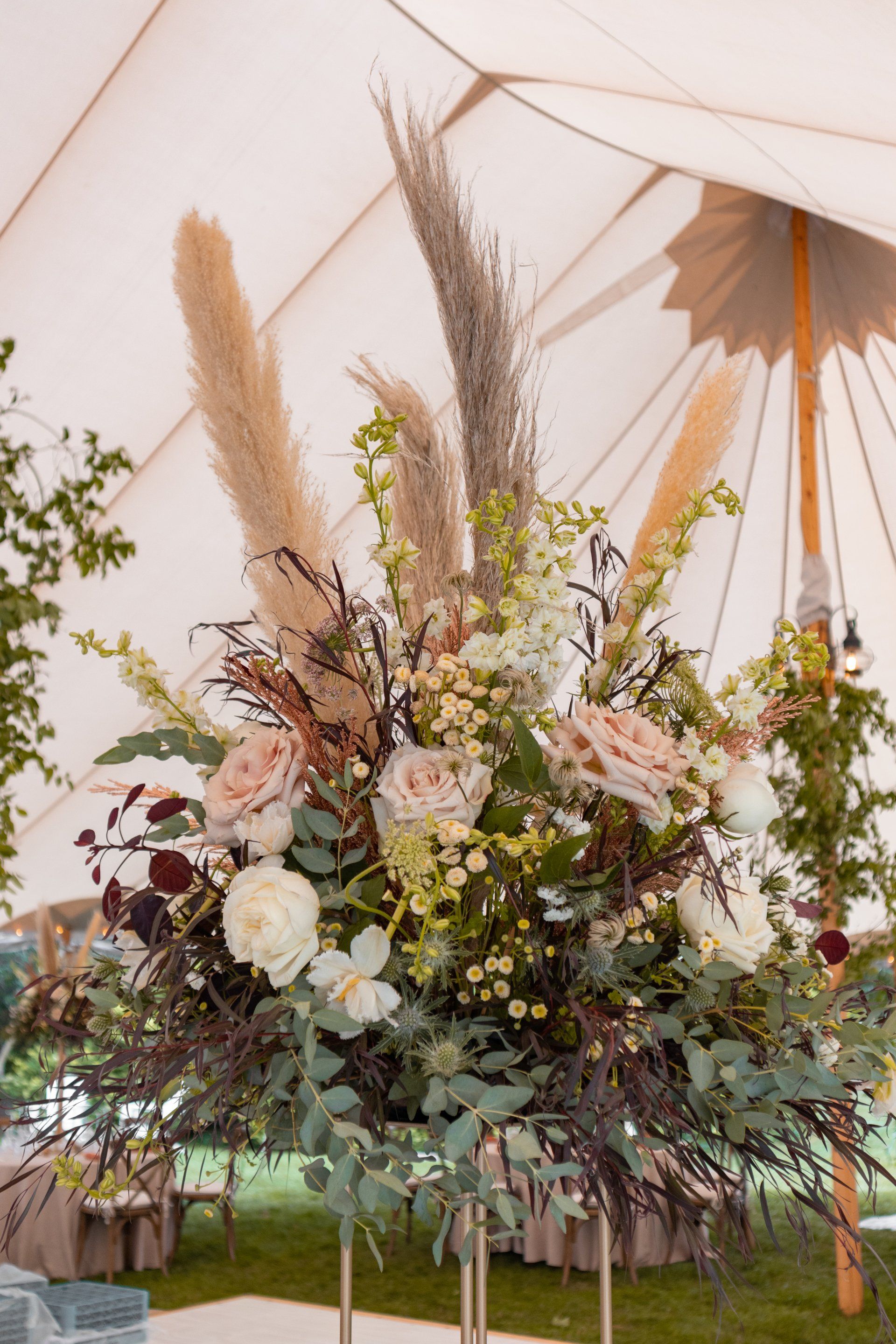 Tall floral arrangement with cream, blush, and greenery under a white tent