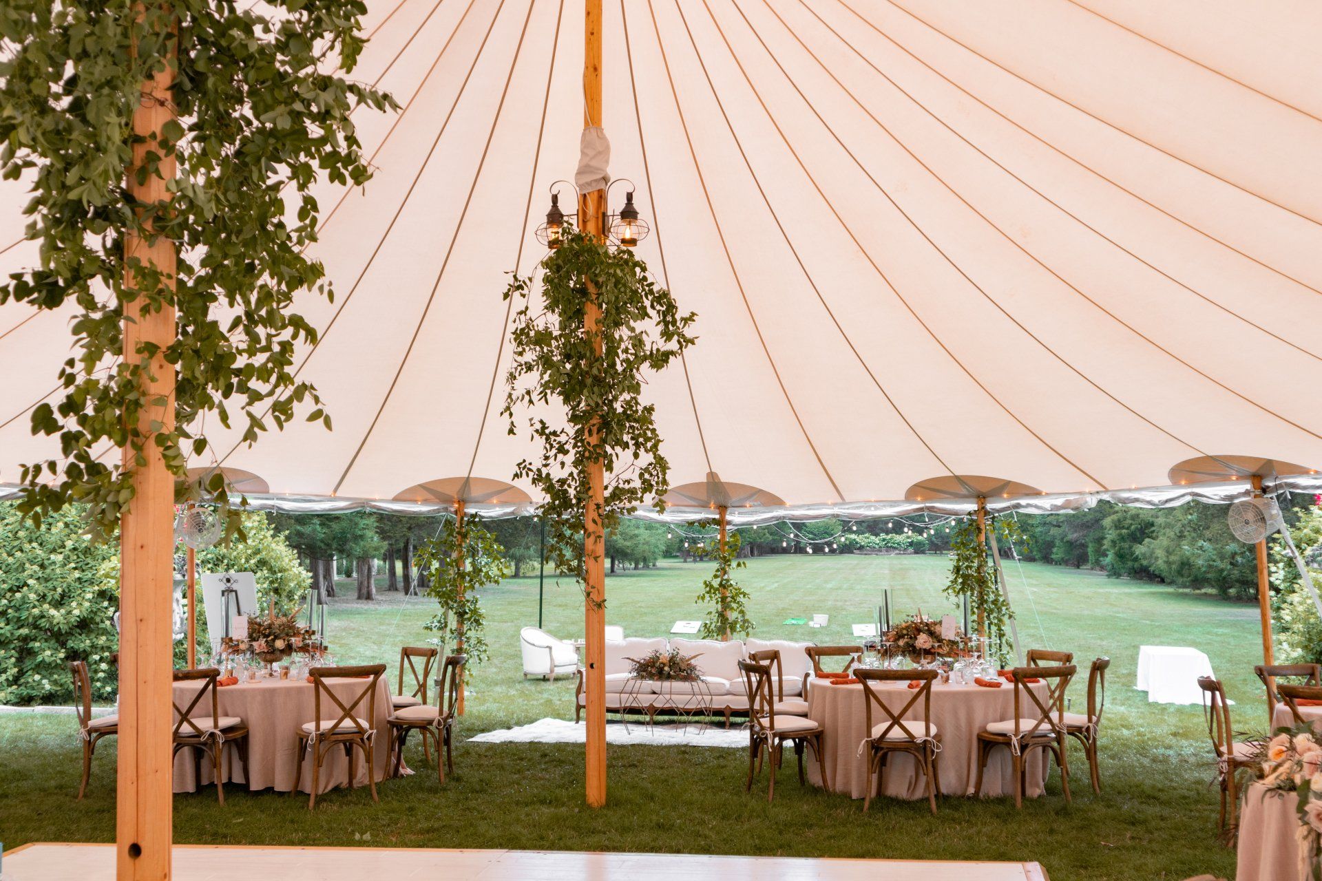 Elegant outdoor tent reception with round tables, wooden chairs, and lake views beyond the lawn