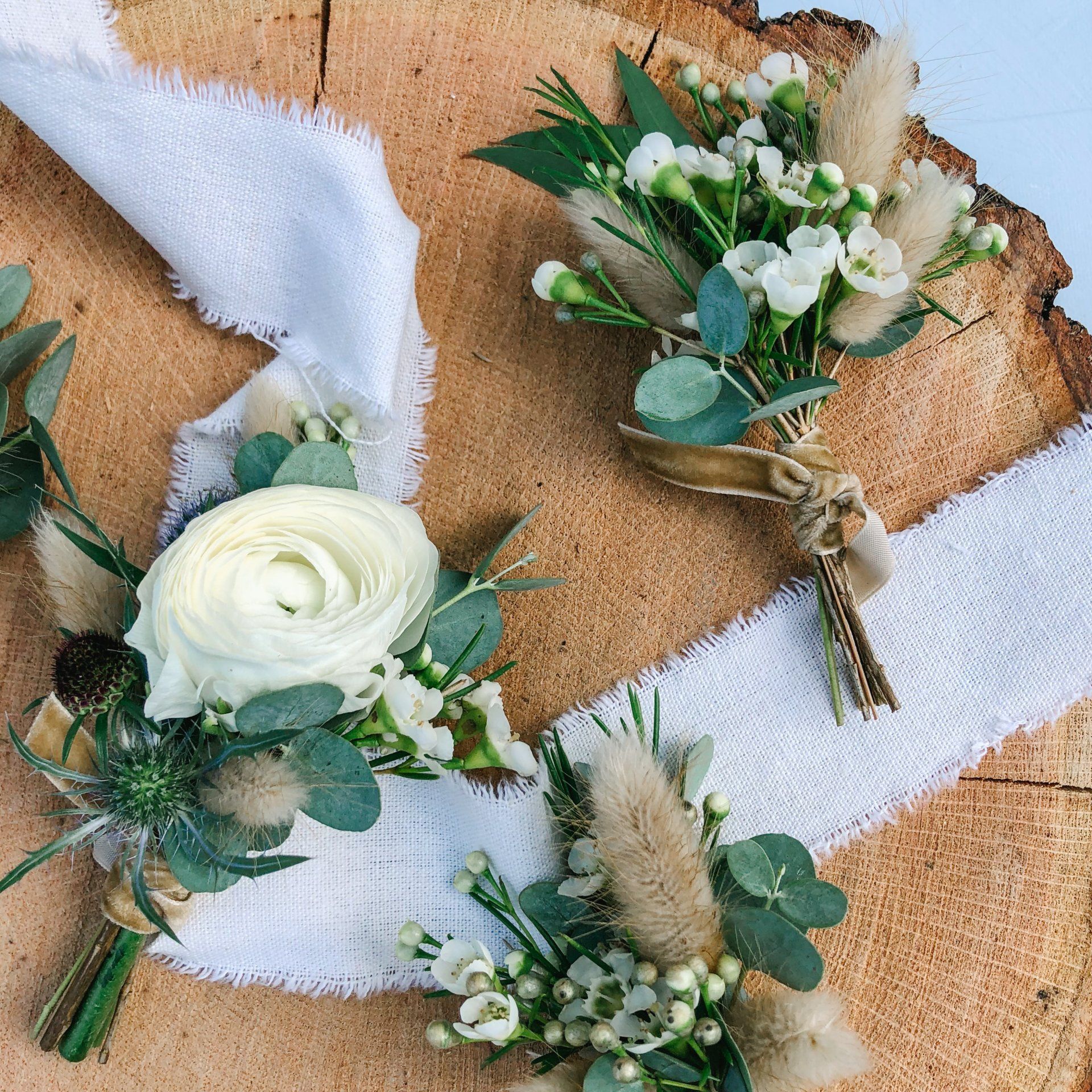 Three white and green floral boutonniere arrangements on a rustic wood background