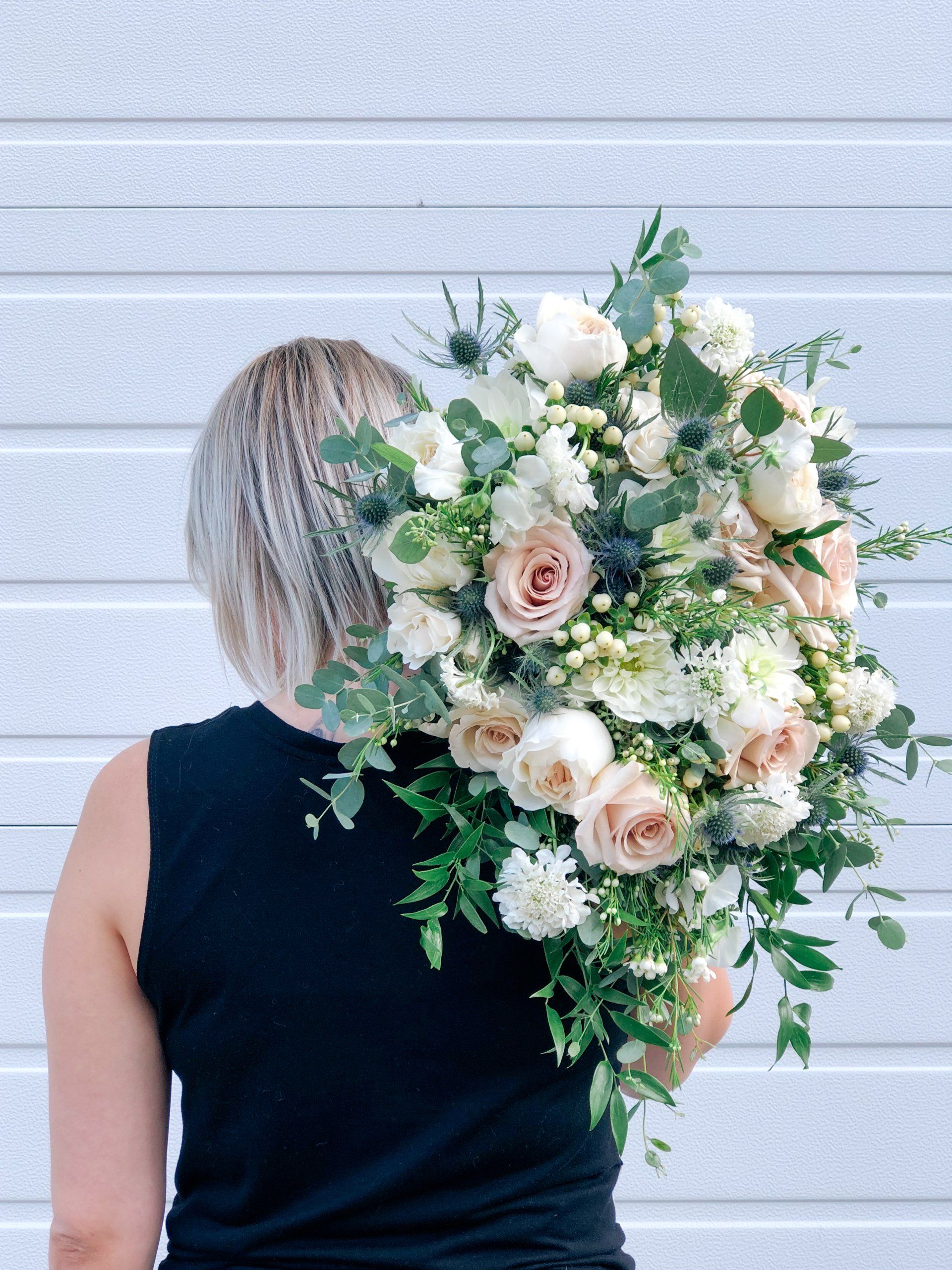 Person with short blonde hair holding a large bouquet of white and blush flowers over one shoulder
