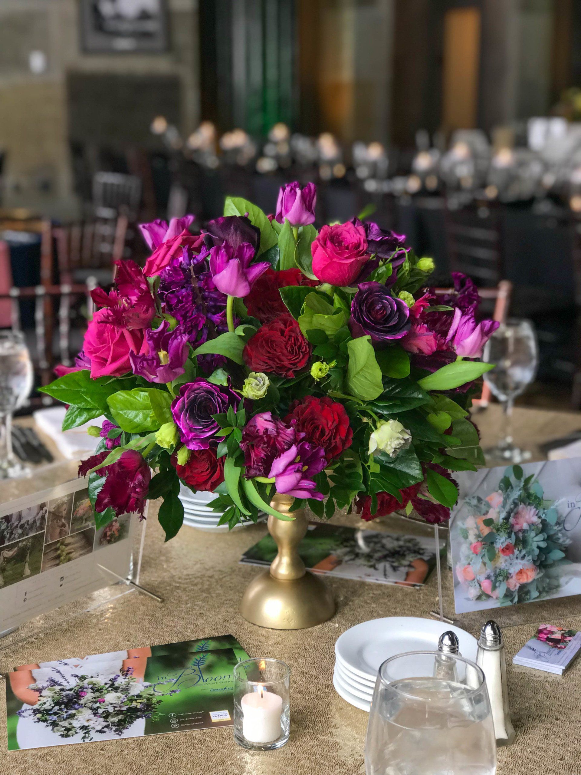 Magenta floral centerpiece in a gold vase on a set dining table with candles and cards