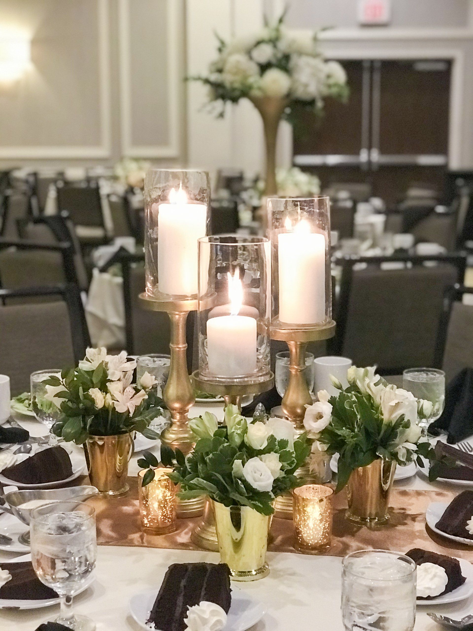 Elegant banquet table with white candles, gold accents, and white floral centerpieces in a reception hall
