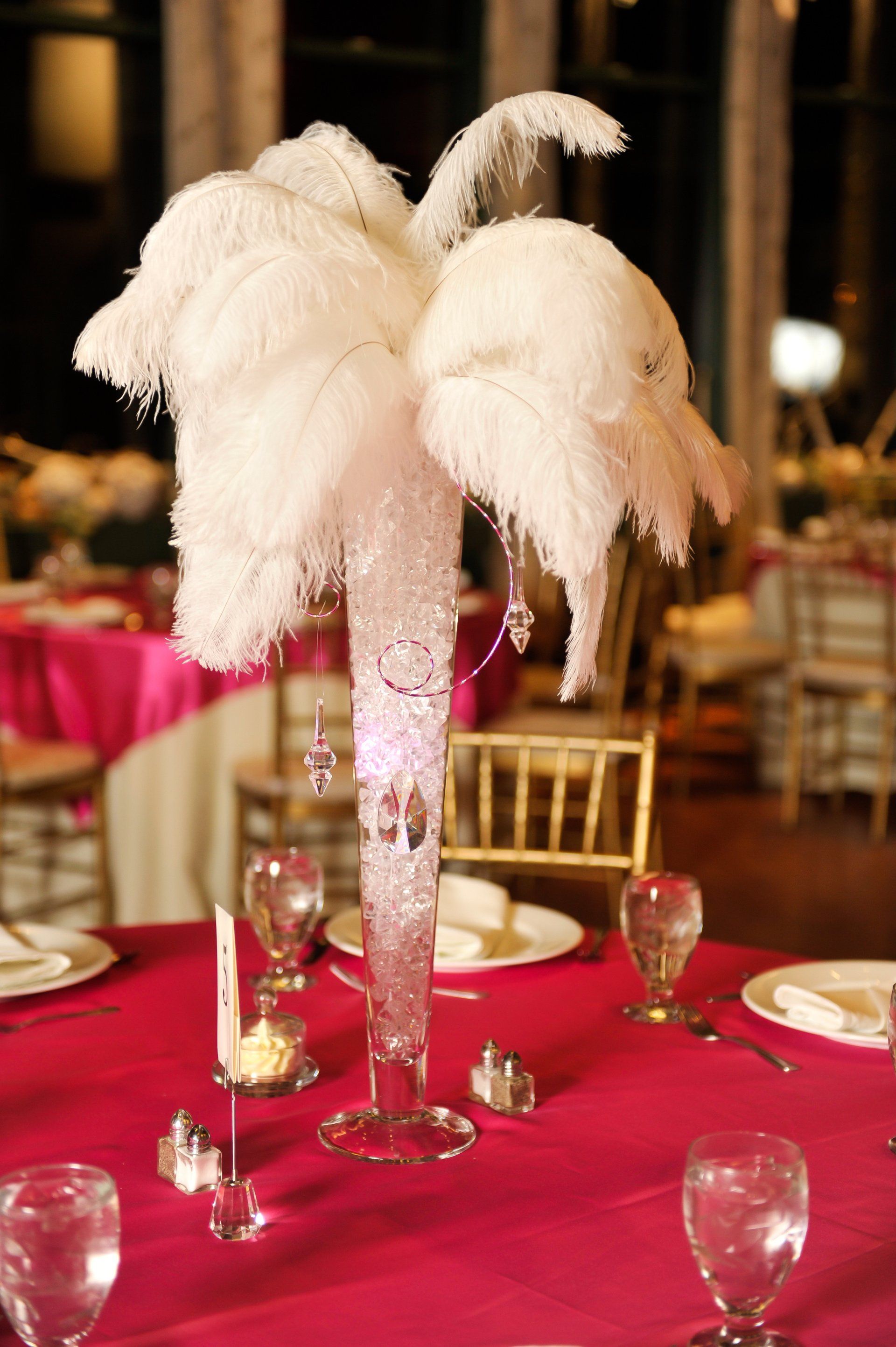 Feather centerpiece in a red tablecloth banquet hall, with candles and wine glasses