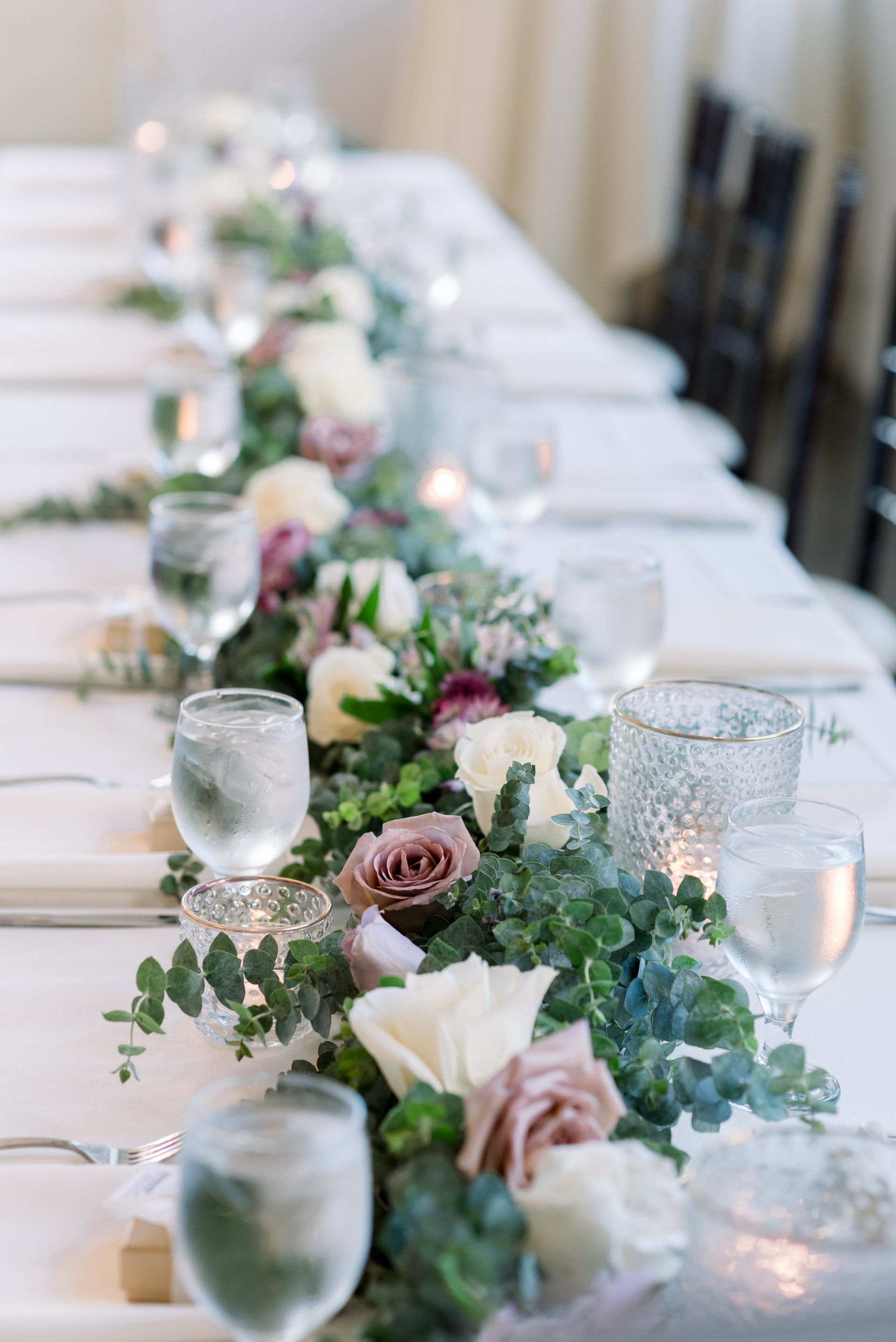 Elegant banquet table with white linens, glassware, and pink floral garland centerpiece