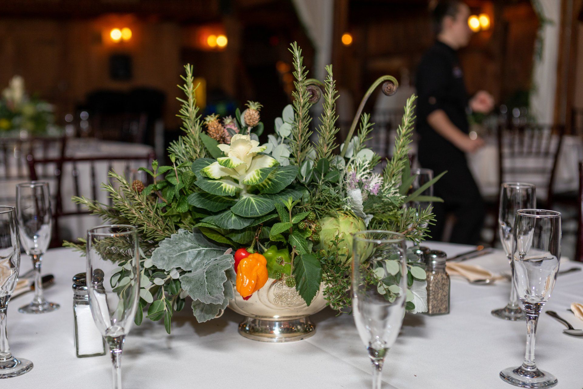 Floral centerpiece on a banquet table with glassware in a warmly lit event hall
