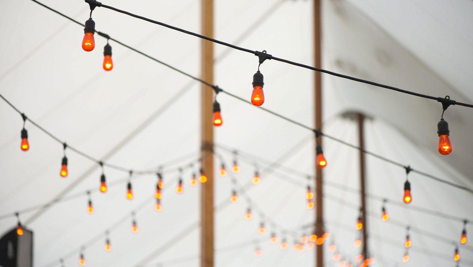 Warm string lights hanging outdoors against a pale sky and blurred wooden poles