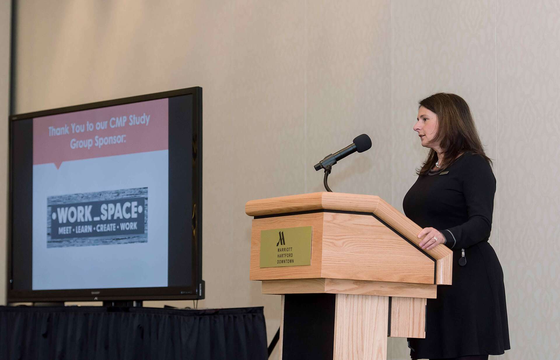 Woman speaking at a podium beside a screen showing a “Work-Study” presentation slide
