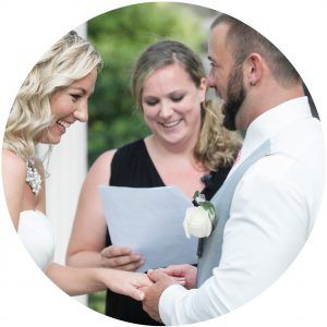 Wedding couple exchanging vows during an outdoor ceremony with an officiant holding the script.