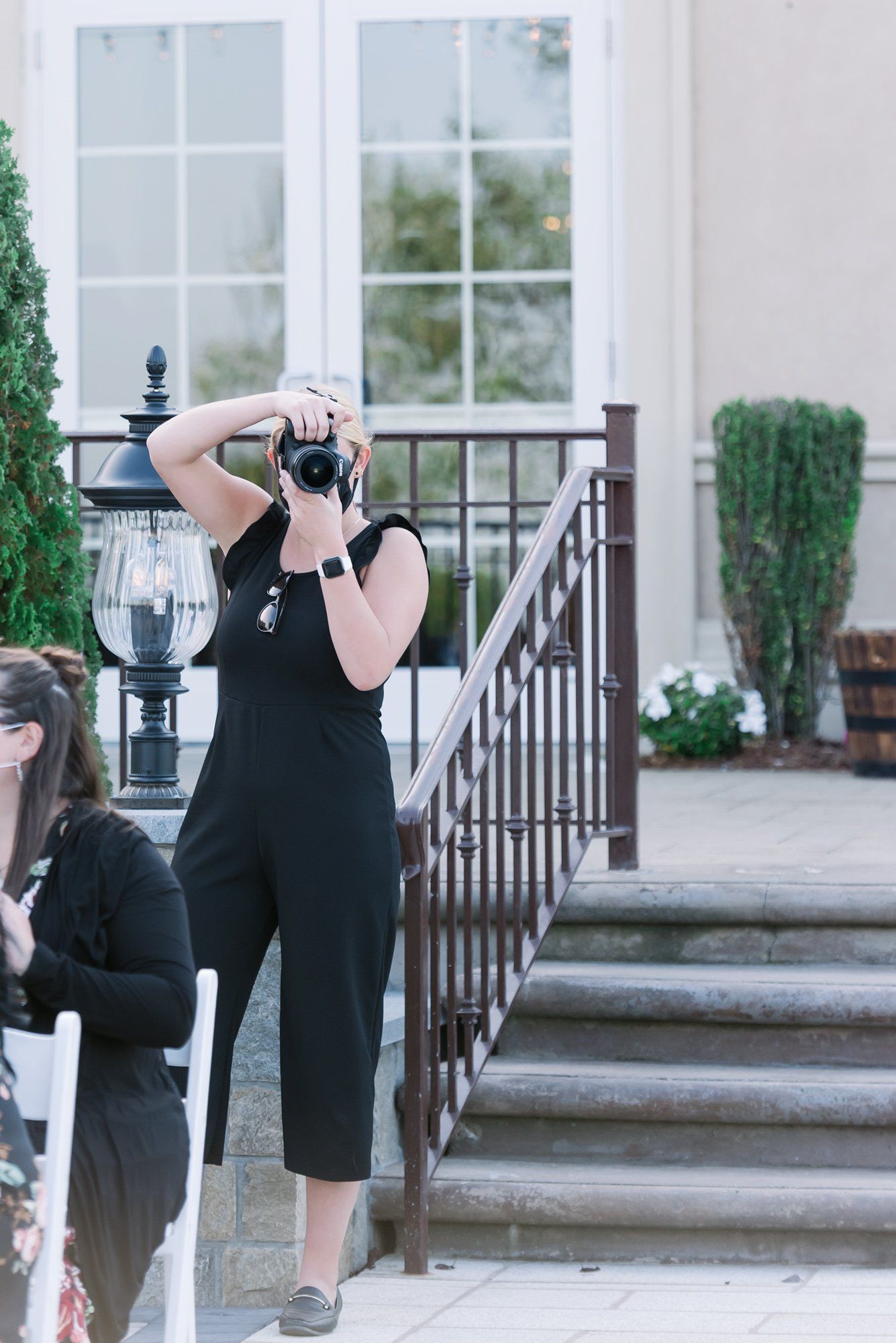 Photographer in black taking a photo outdoors beside steps and a white building