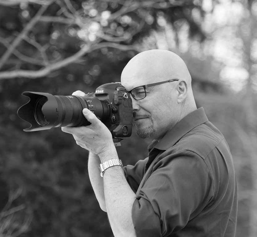 Photographer aiming a DSLR with telephoto lens outdoors in black and white