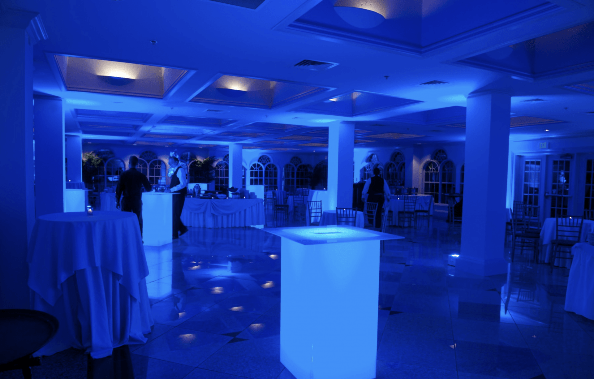 Blue-lit banquet hall with cocktail tables and guests in the background