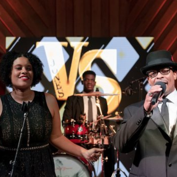 Three musicians performing on stage, with a singer in a black dress and a man in a suit holding a microphone.