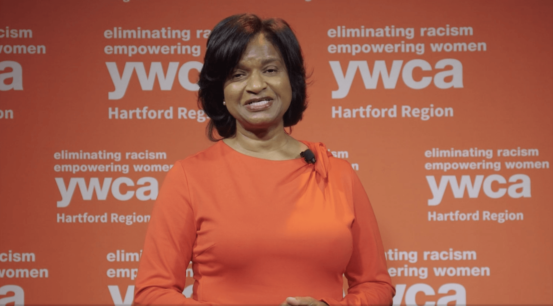 Woman in orange top smiling at a YWCA Hartford Region event backdrop