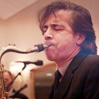Musician playing saxophone with eyes closed on a warmly lit stage