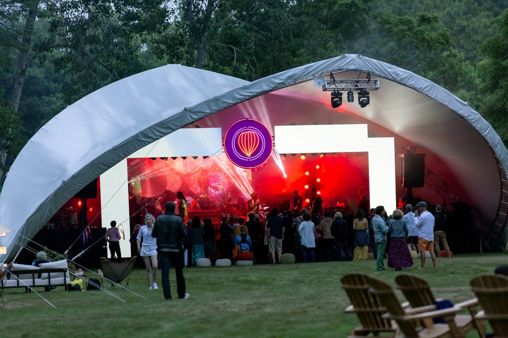 Outdoor concert under a white tent with red stage lights and a crowd watching on the lawn