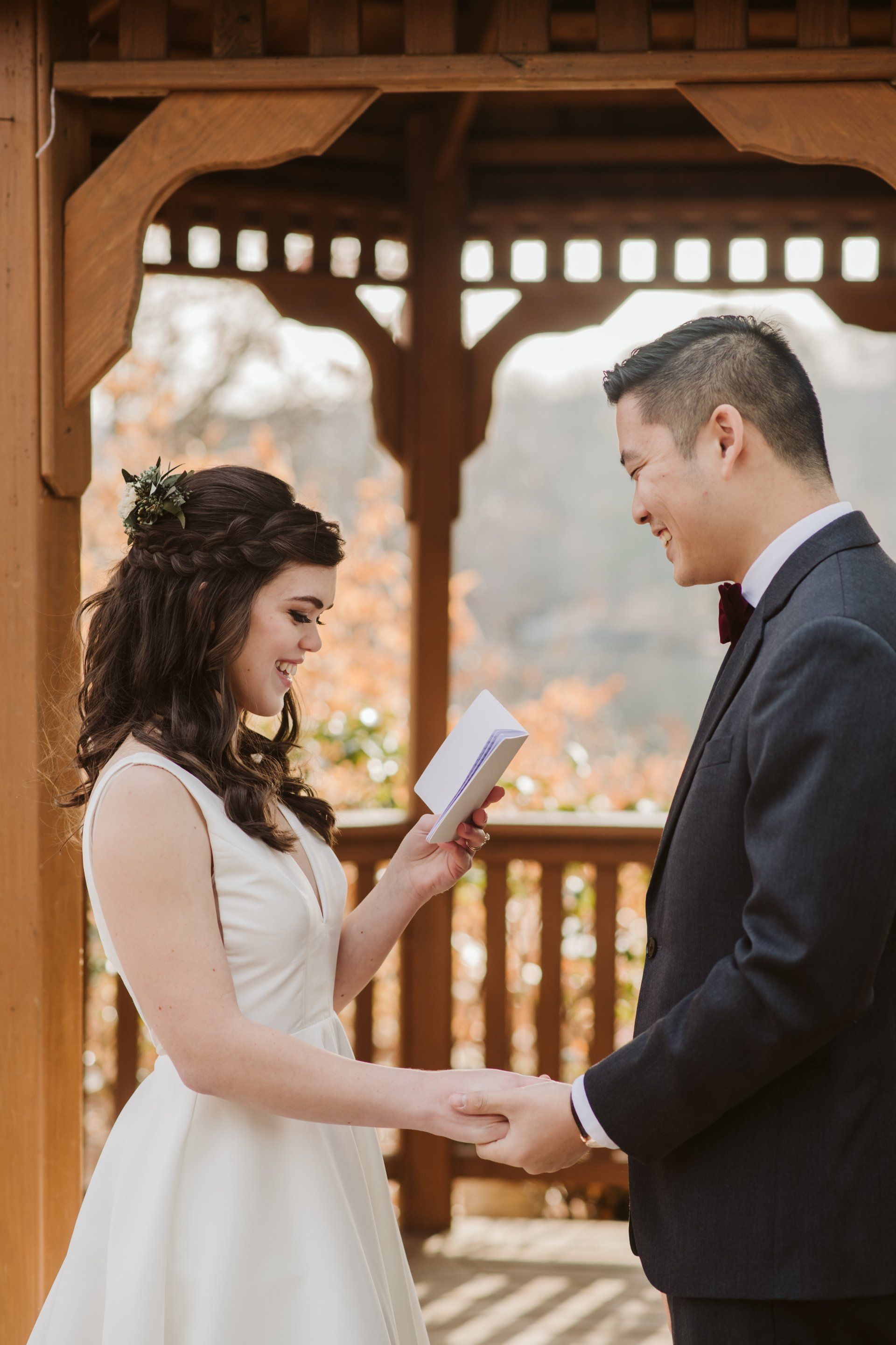 Couple exchanging vows under a wooden gazebo at an outdoor wedding ceremony