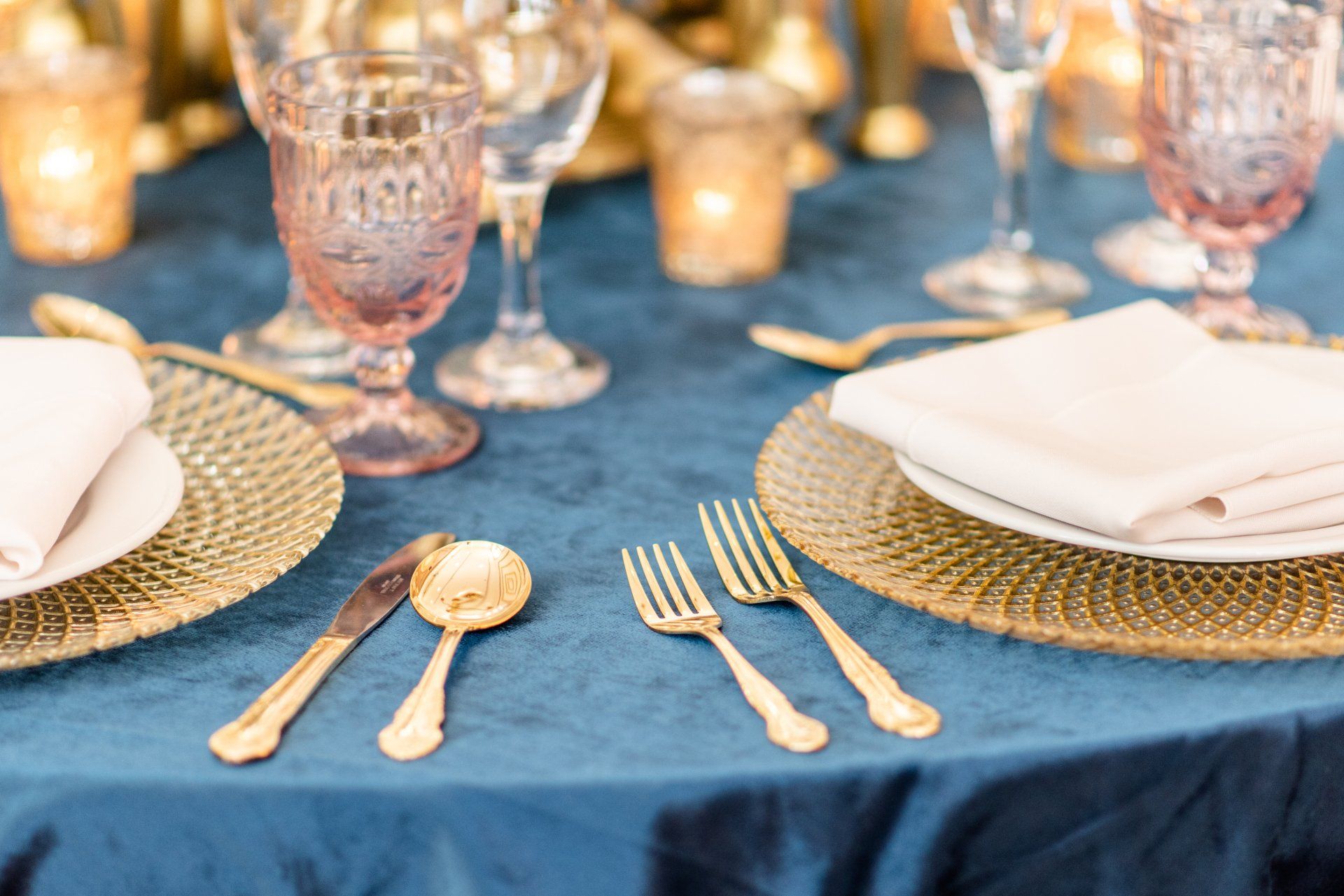 Elegant table setting with gold flatware, white napkins, and crystal glasses on a blue tablecloth