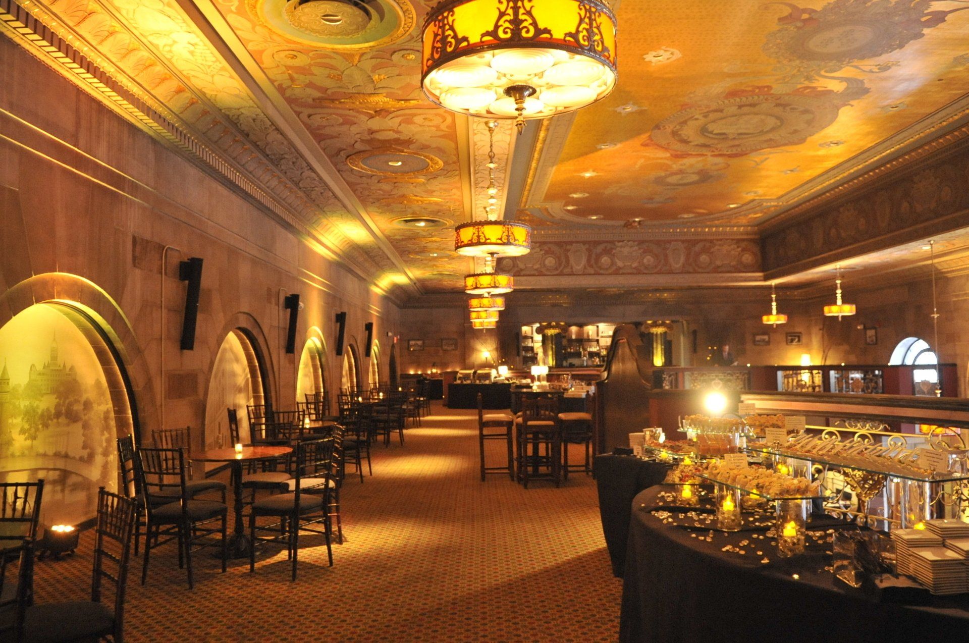 Elegant banquet hall with chandeliers, arched windows, and a buffet table set for an event