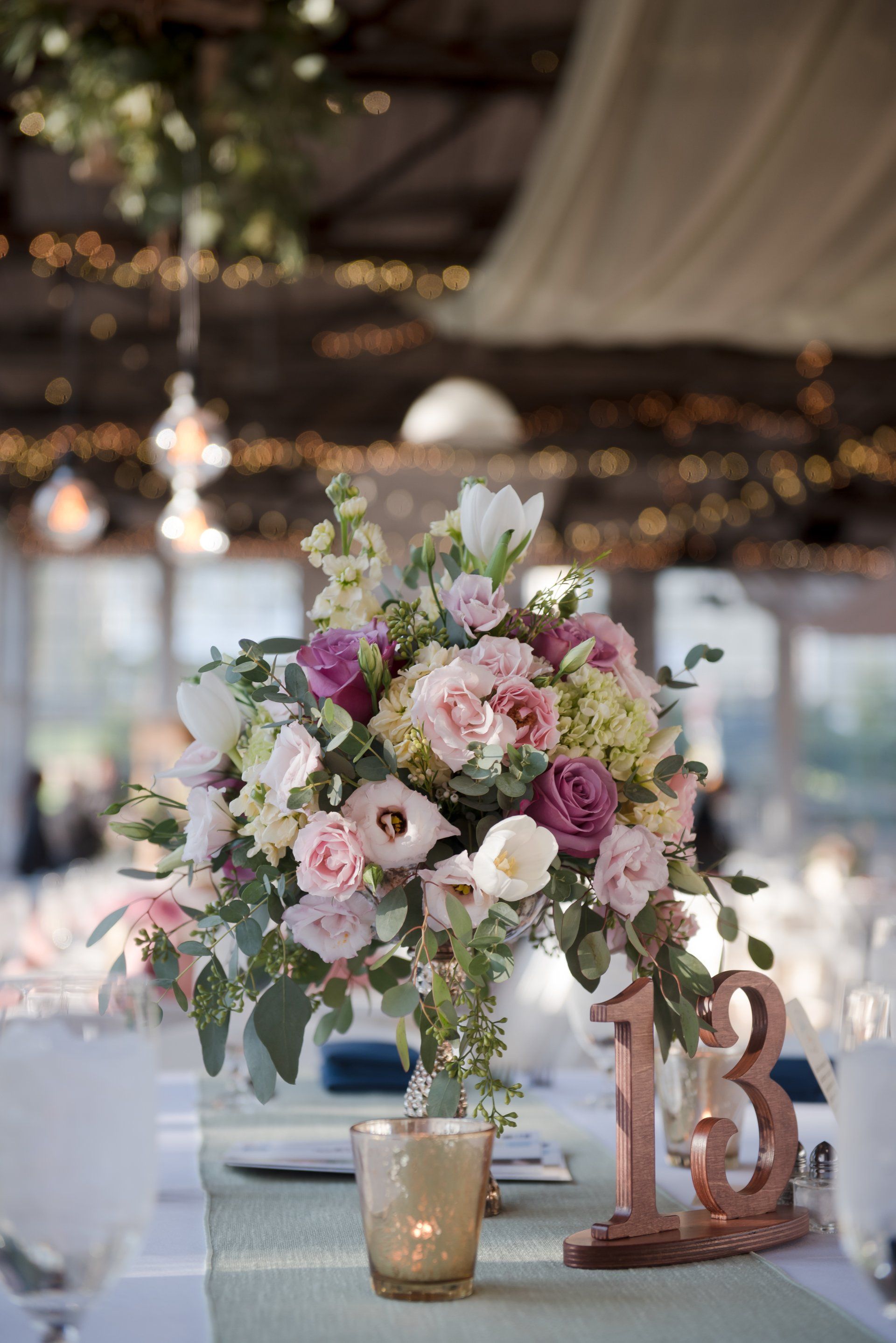 Floral centerpiece with pastel flowers, candle, and table number 13 at a decorated event table